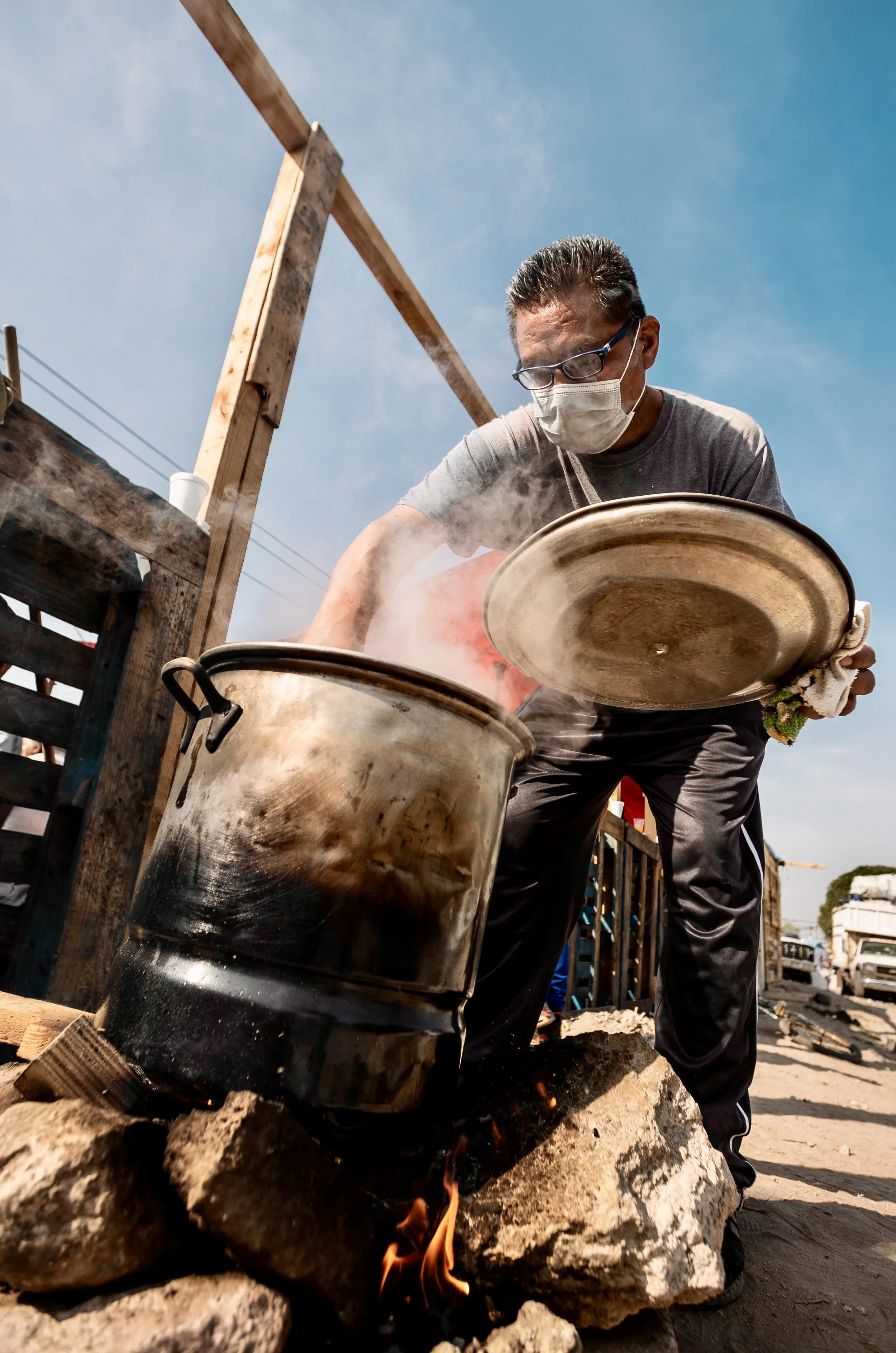 Masked man cooking in a large metal pot over an open fire outdoors in Mexico City. Photo by David Ferry Jr.