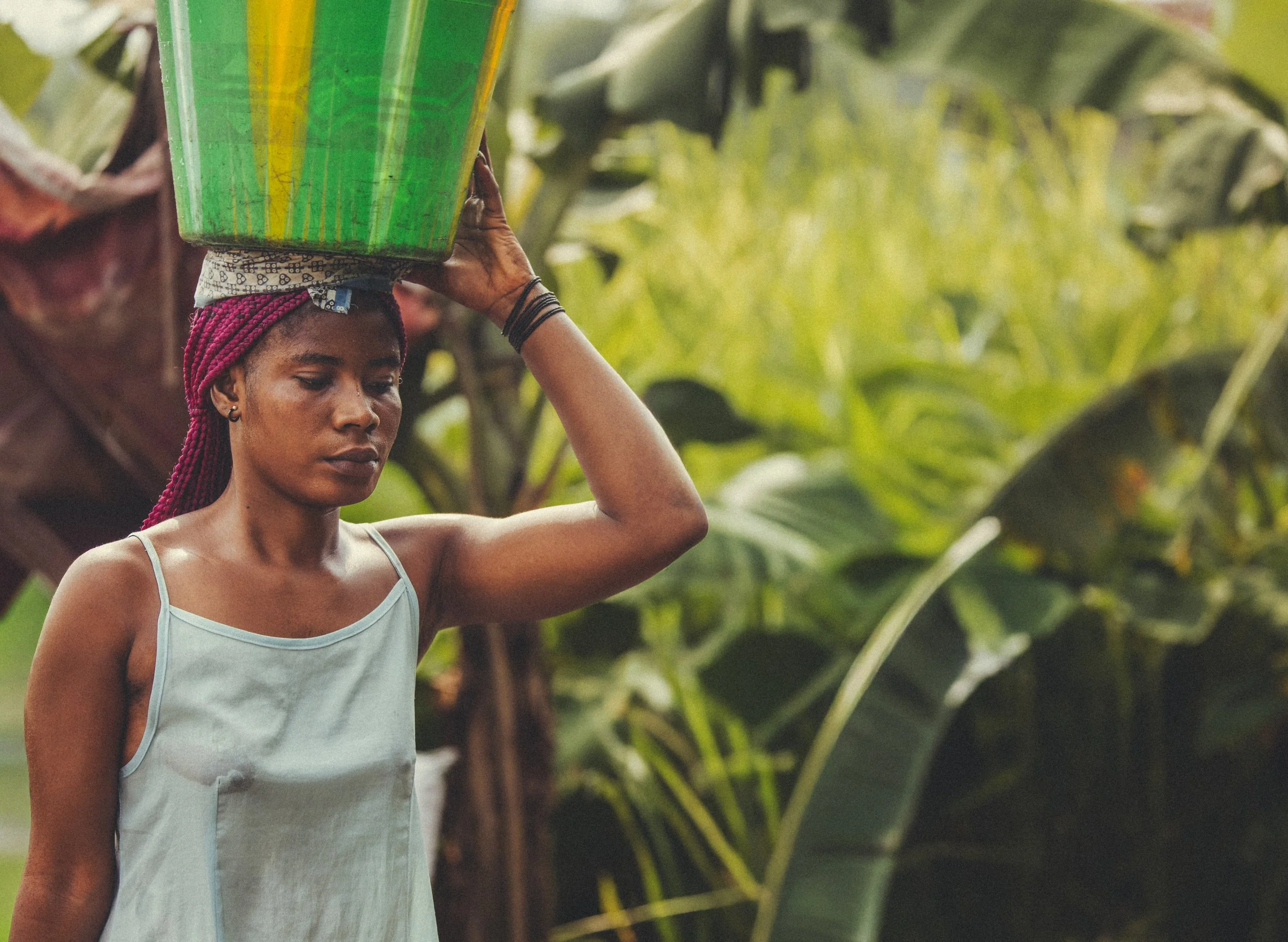 Woman carrying a green and yellow container on her head in a tropical forest in Congo. Photo by David Ferry Jr.