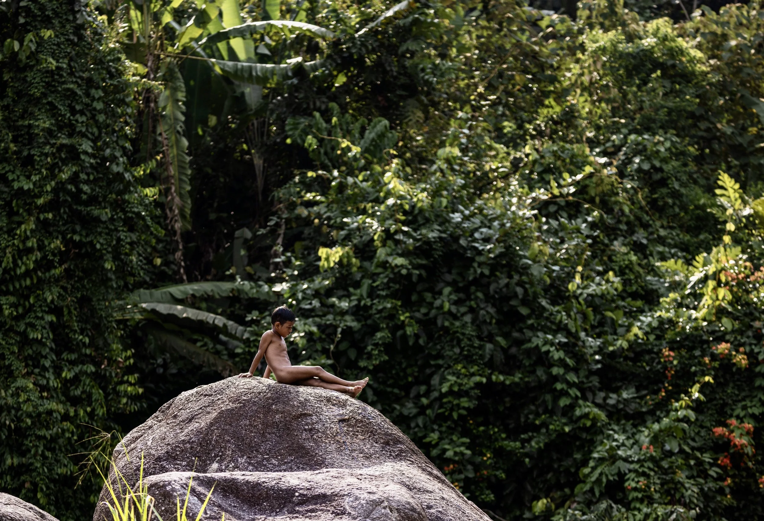 Malaysian child sitting on a large rock in a lush tropical jungle. Photo by David Ferry Jr.