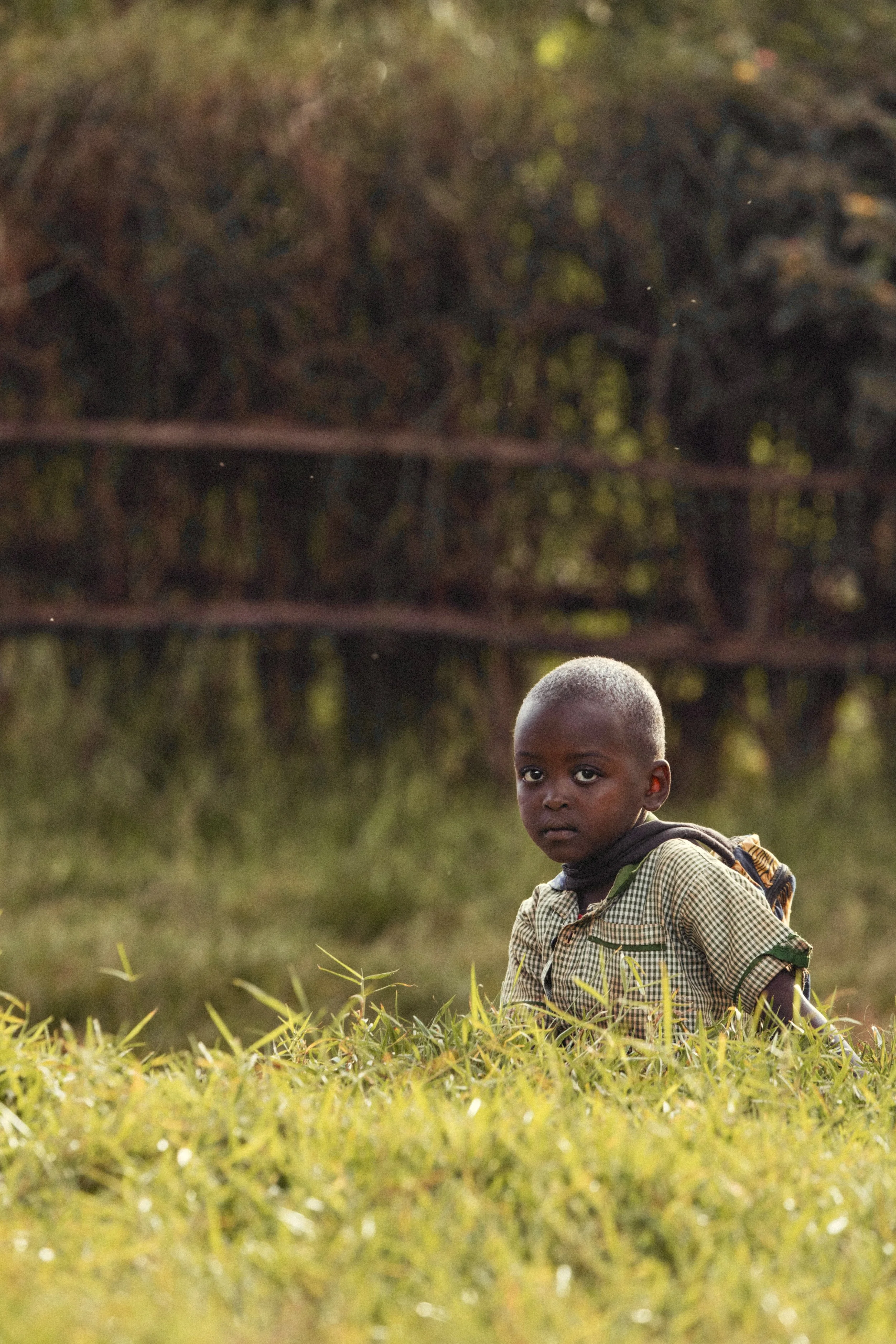 Young child wearing a backpack standing in tall grass outdoors in Rwanda. Photo by David Ferry Jr.