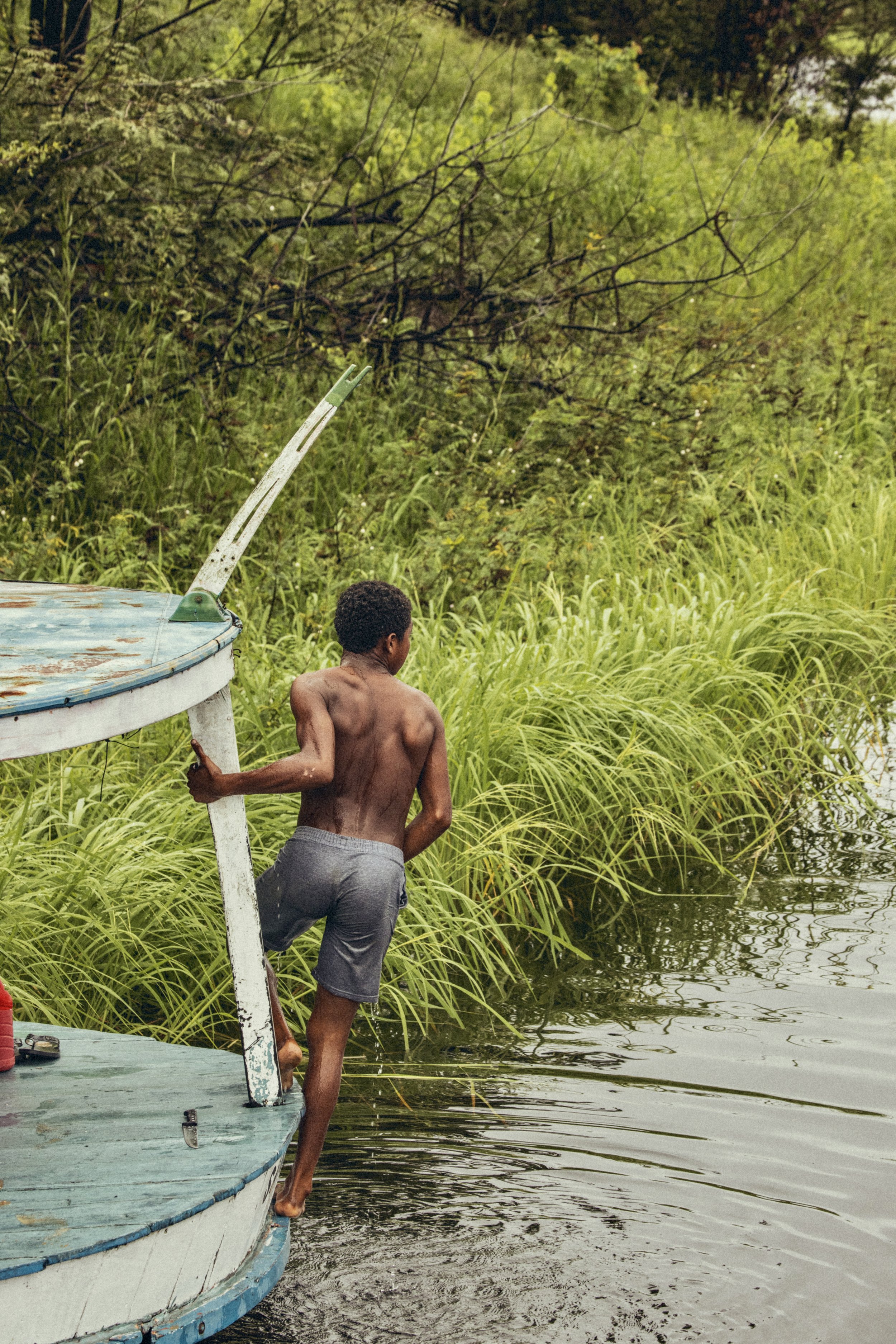 Man propelling a small wooden boat through a lush, grassy riverbank in the Brazilian Amazon. Photo by David Ferry Jr.