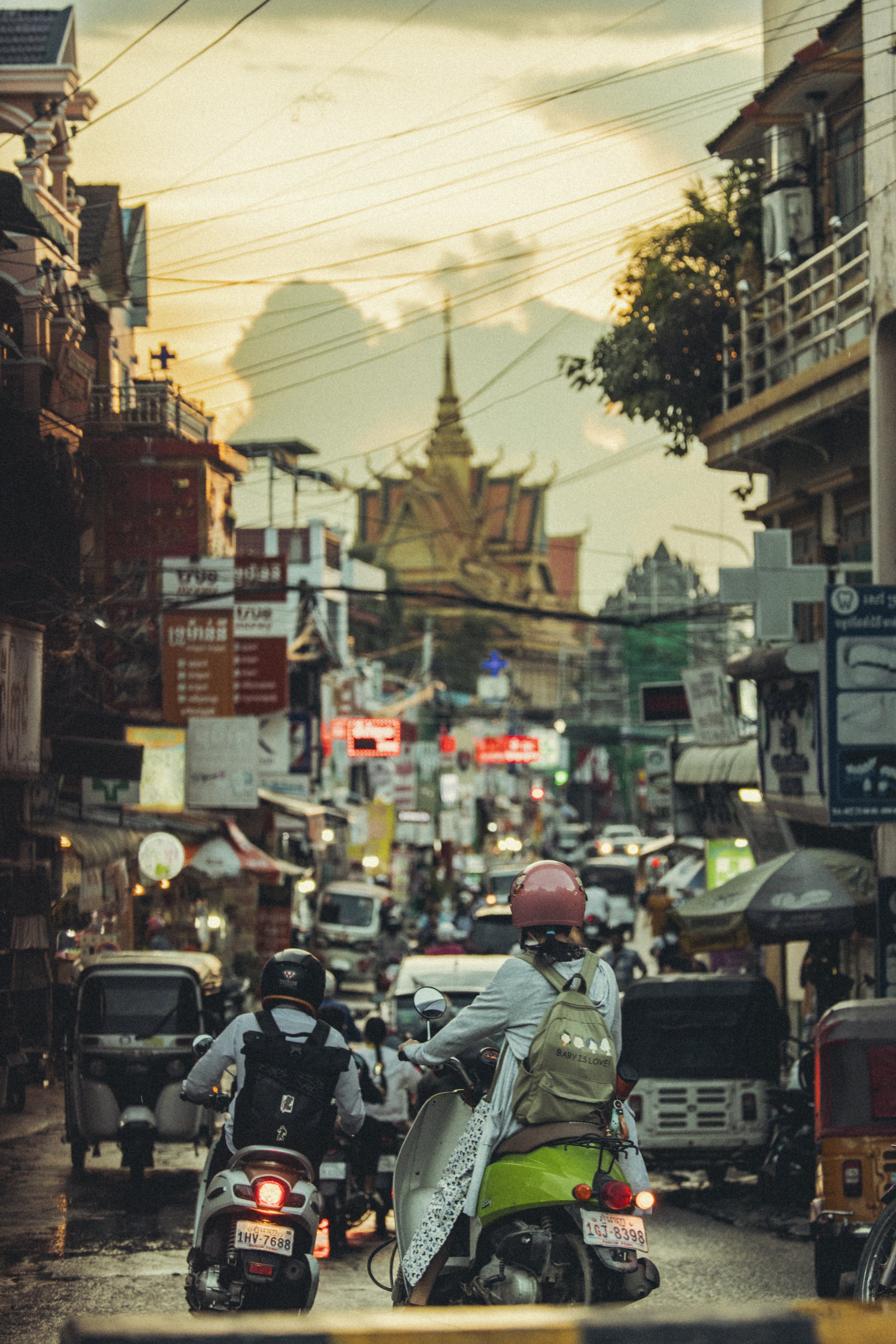 Busy Cambodian city street with motorbikes, cars, storefronts, overhead utility wires, and urban buildings at dusk. Photo by David Ferry Jr.
