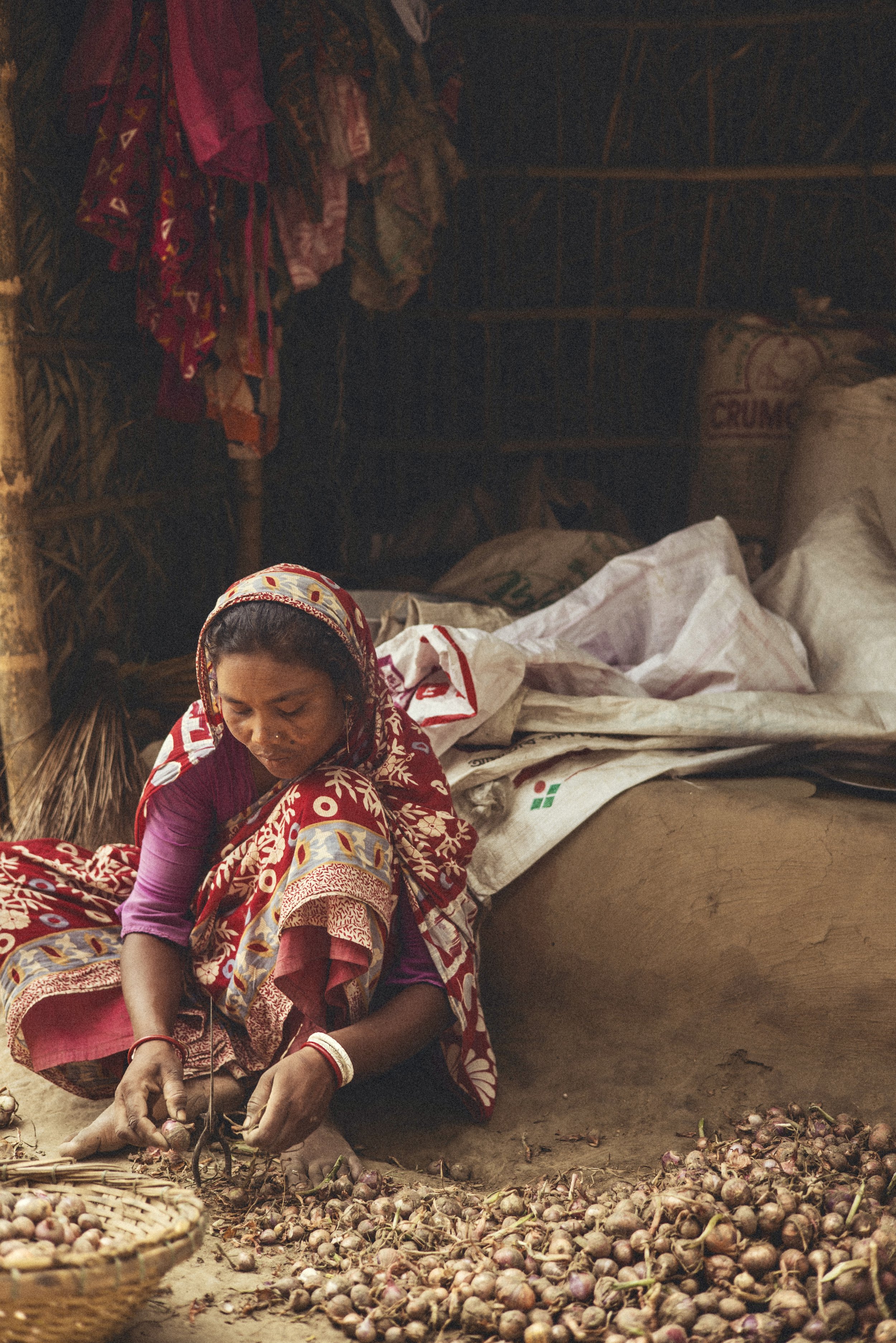 Woman in a colorful sari sorting onions by hand on a dirt floor in a rustic storage room in Bangladesh. Photo by David Ferry Jr.