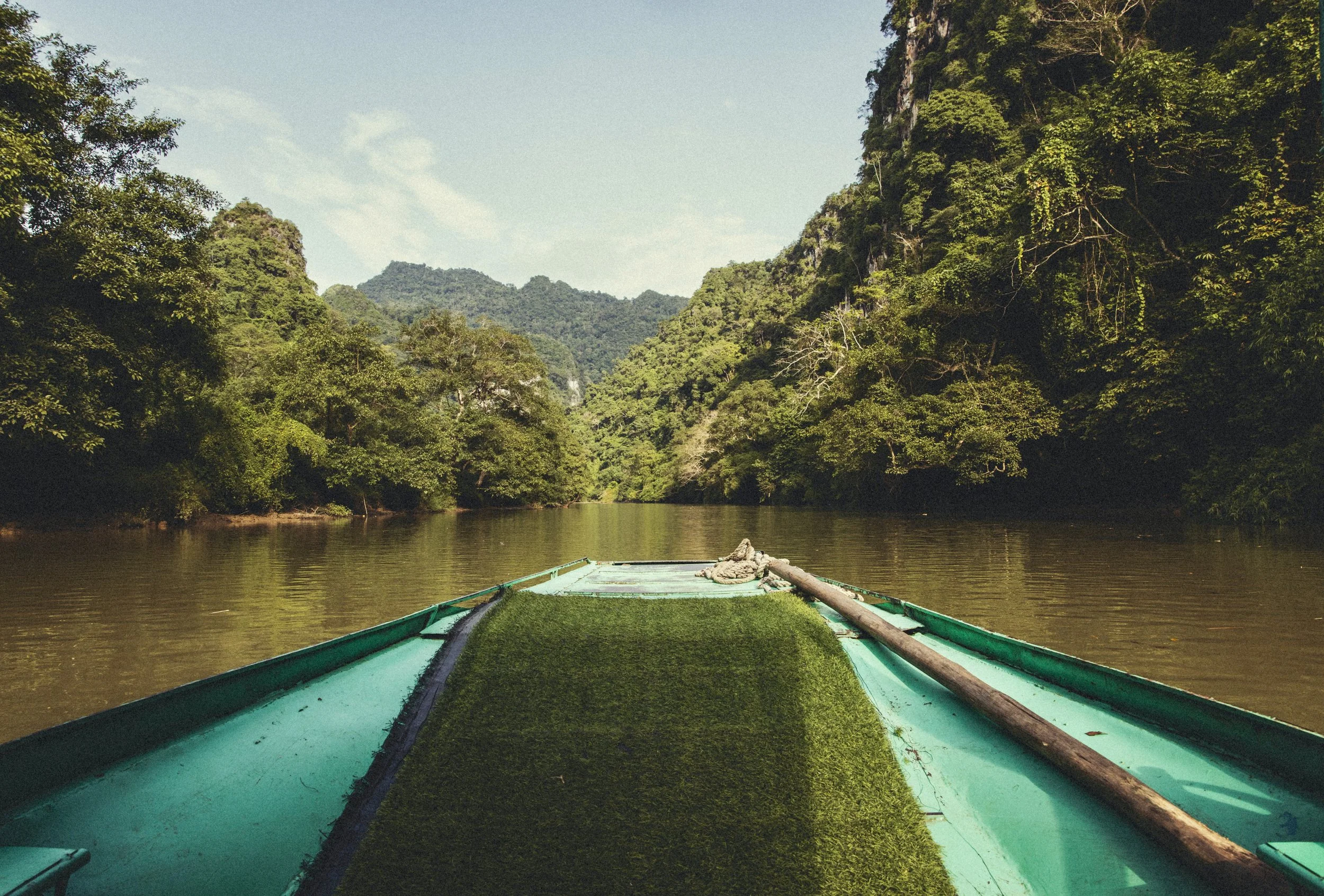 View from a small green boat across a calm jungle lake toward lush, forest-covered karst cliffs and mountains in northern Vietnam. Photo by David Ferry Jr.