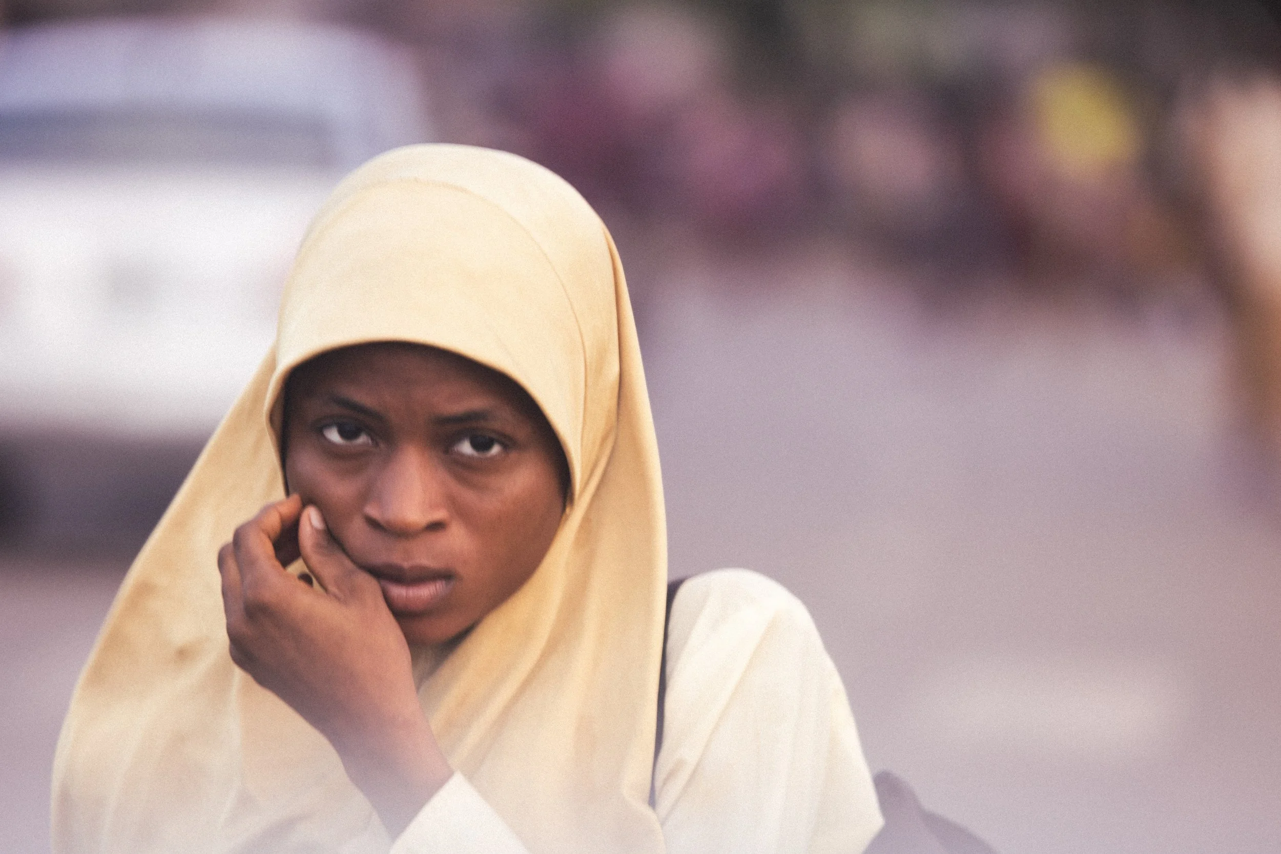 Young Black woman wearing a beige hijab and white clothing, touching her cheek in Lagos, Nigeria. Photo by David Ferry Jr.
