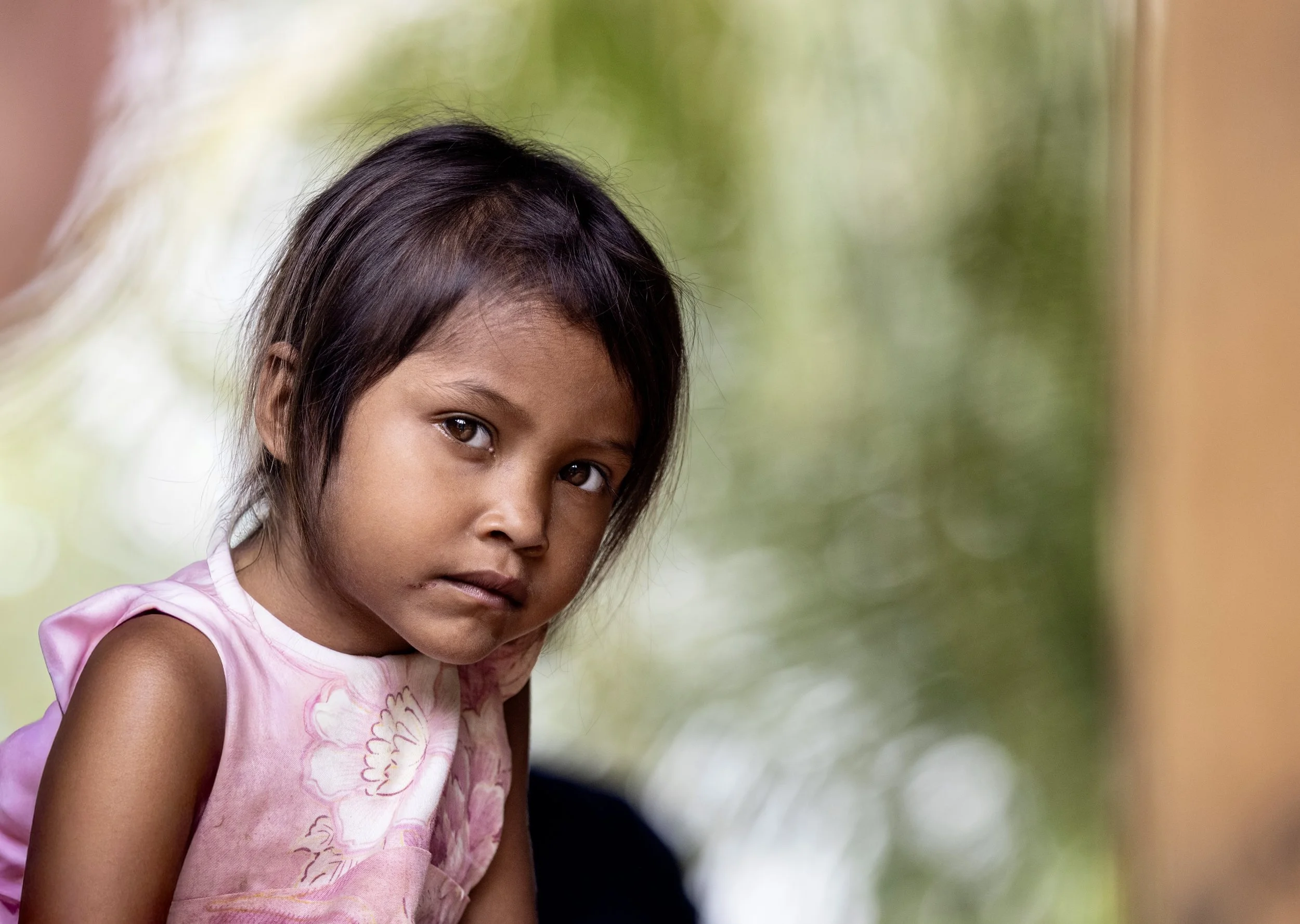 Close-up portrait of a young girl in a pink floral dress looking at the camera in Brazil. Photo by David Ferry Jr.