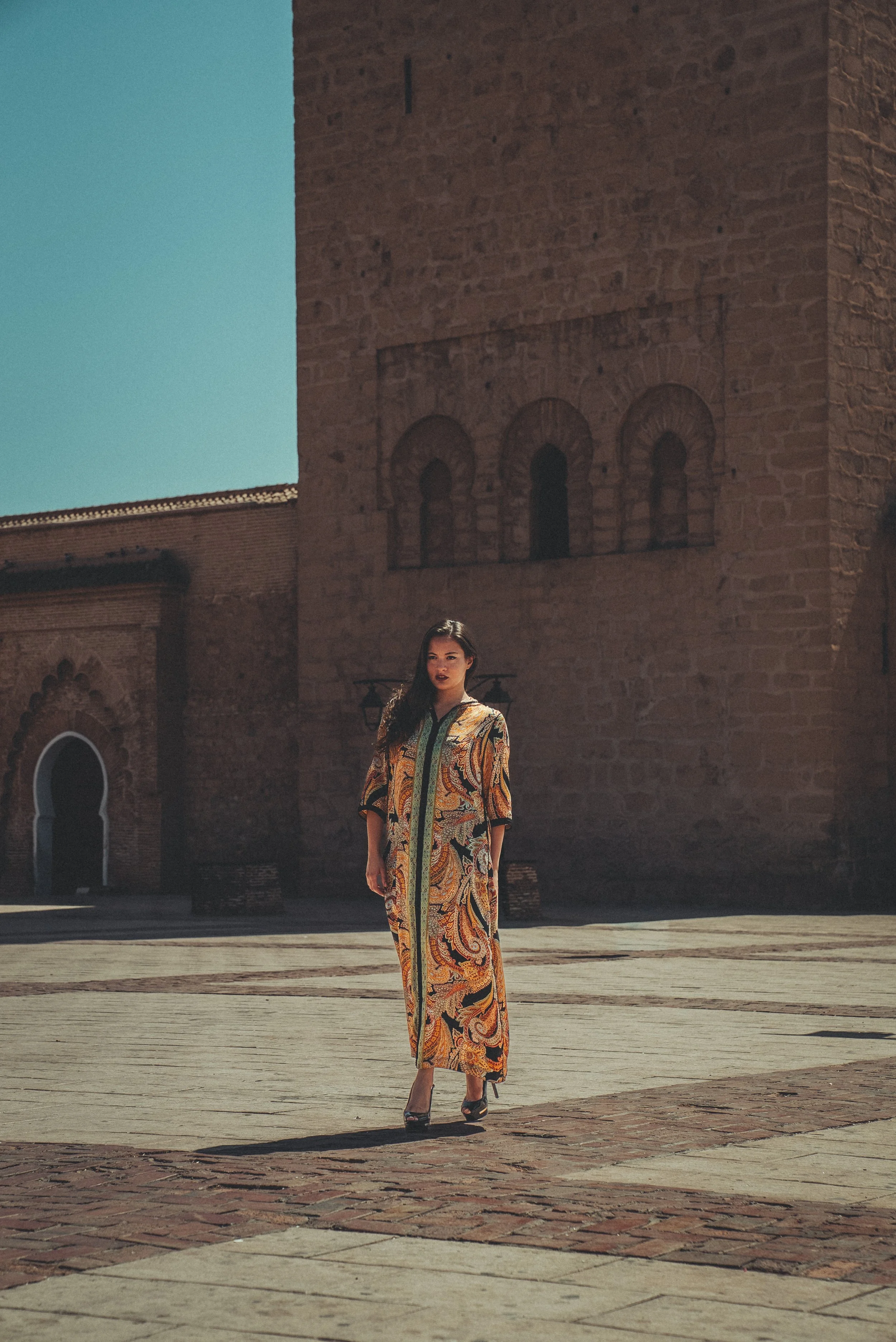 Woman in a colorful paisley dress standing in front of an old brick building with arched doorways in Marrakech, Morocco. Photo by David Ferry Jr.