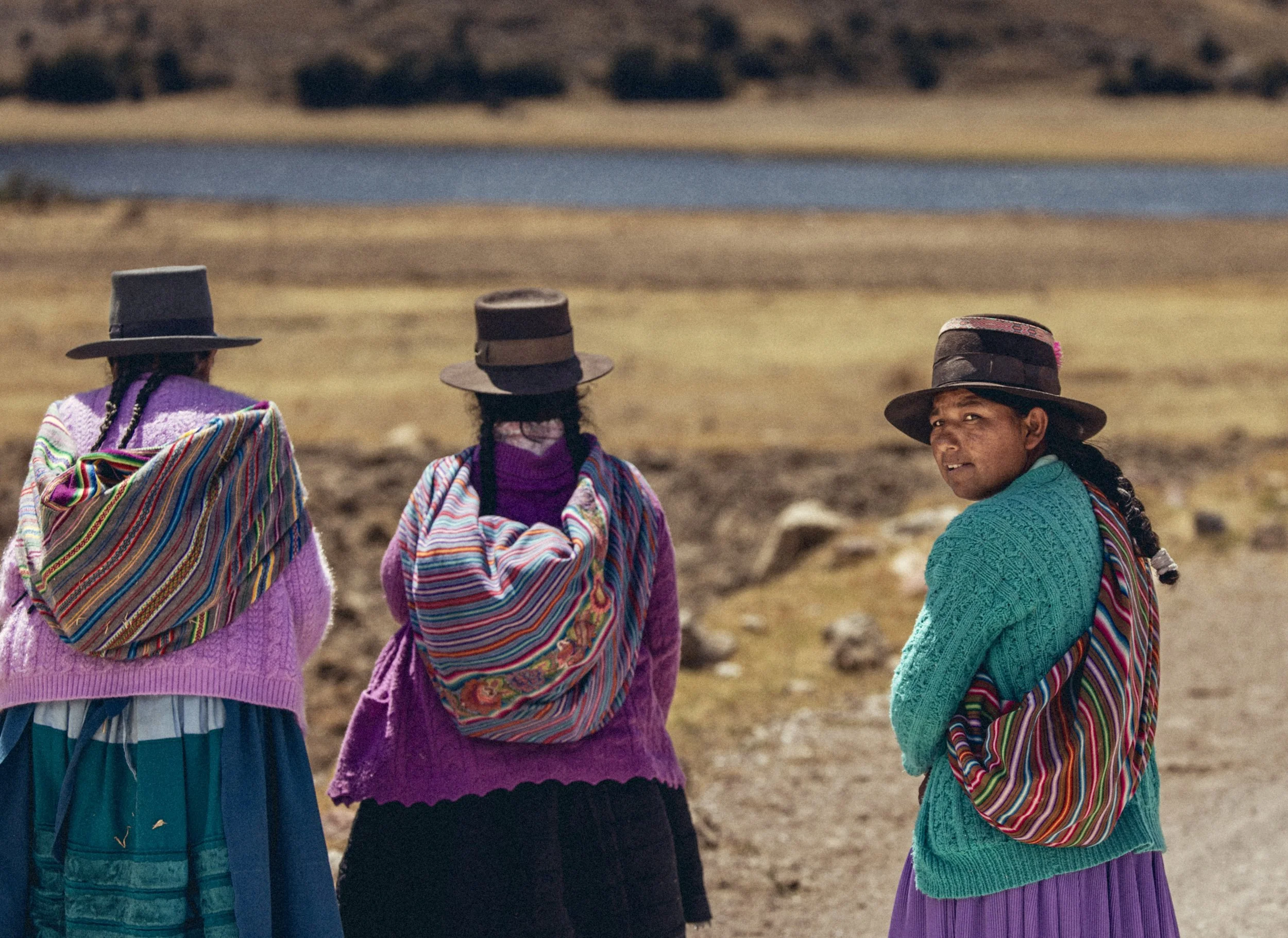Three Indigenous Andean women wearing traditional colorful garments and hats stand in a high-altitude mountain landscape of Peru. Photo by David Ferry Jr.