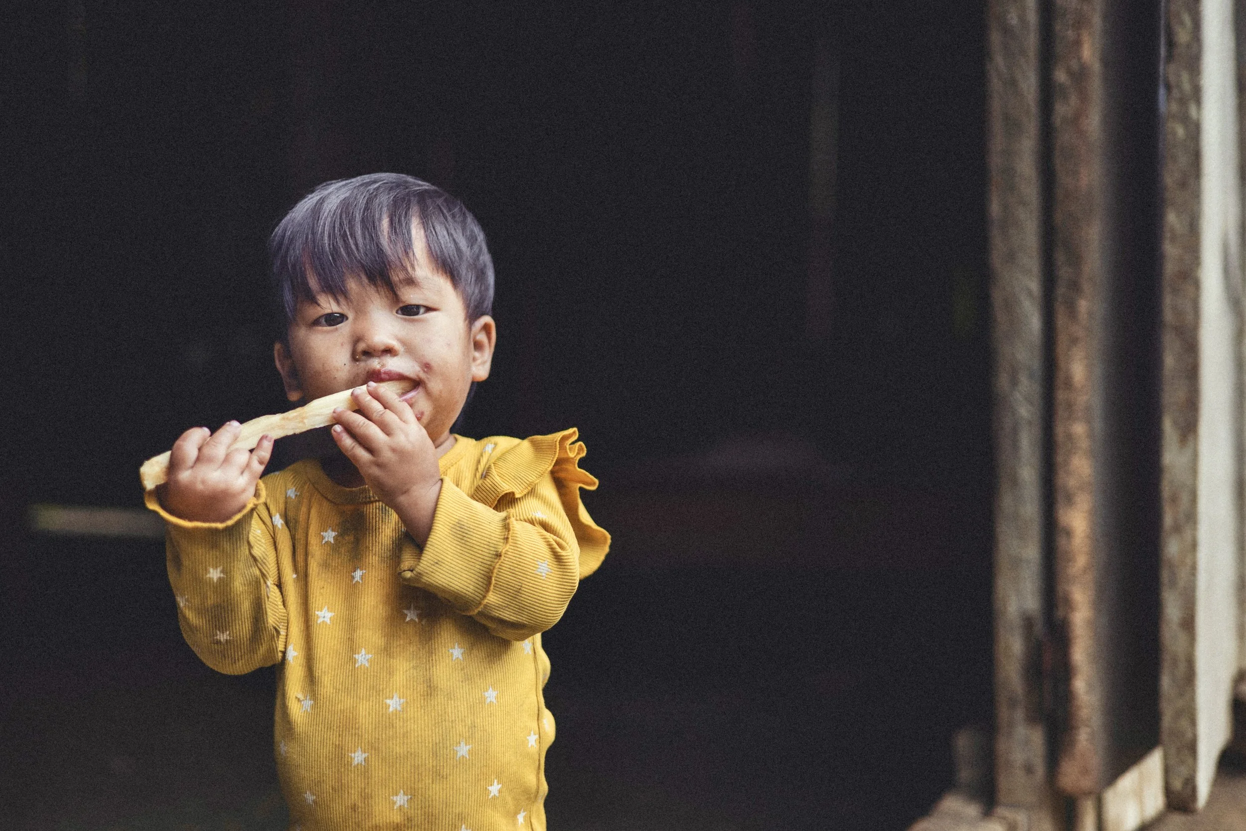 Young child in a yellow star-patterned sweater eating a peeled sugarcane stalk in Vietnam. Photo by David Ferry Jr.