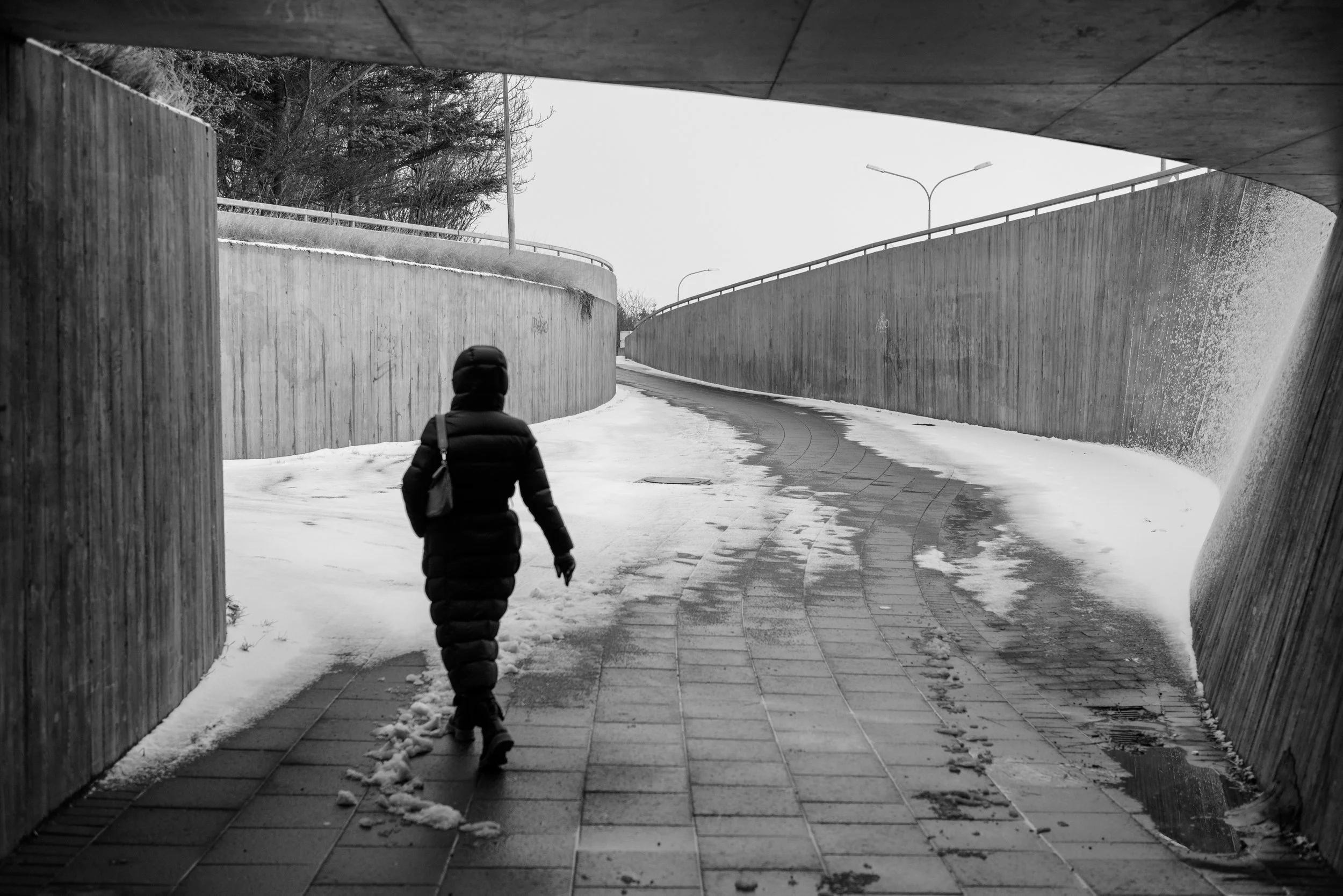 Person in a puffer coat walking through a snowy concrete underpass