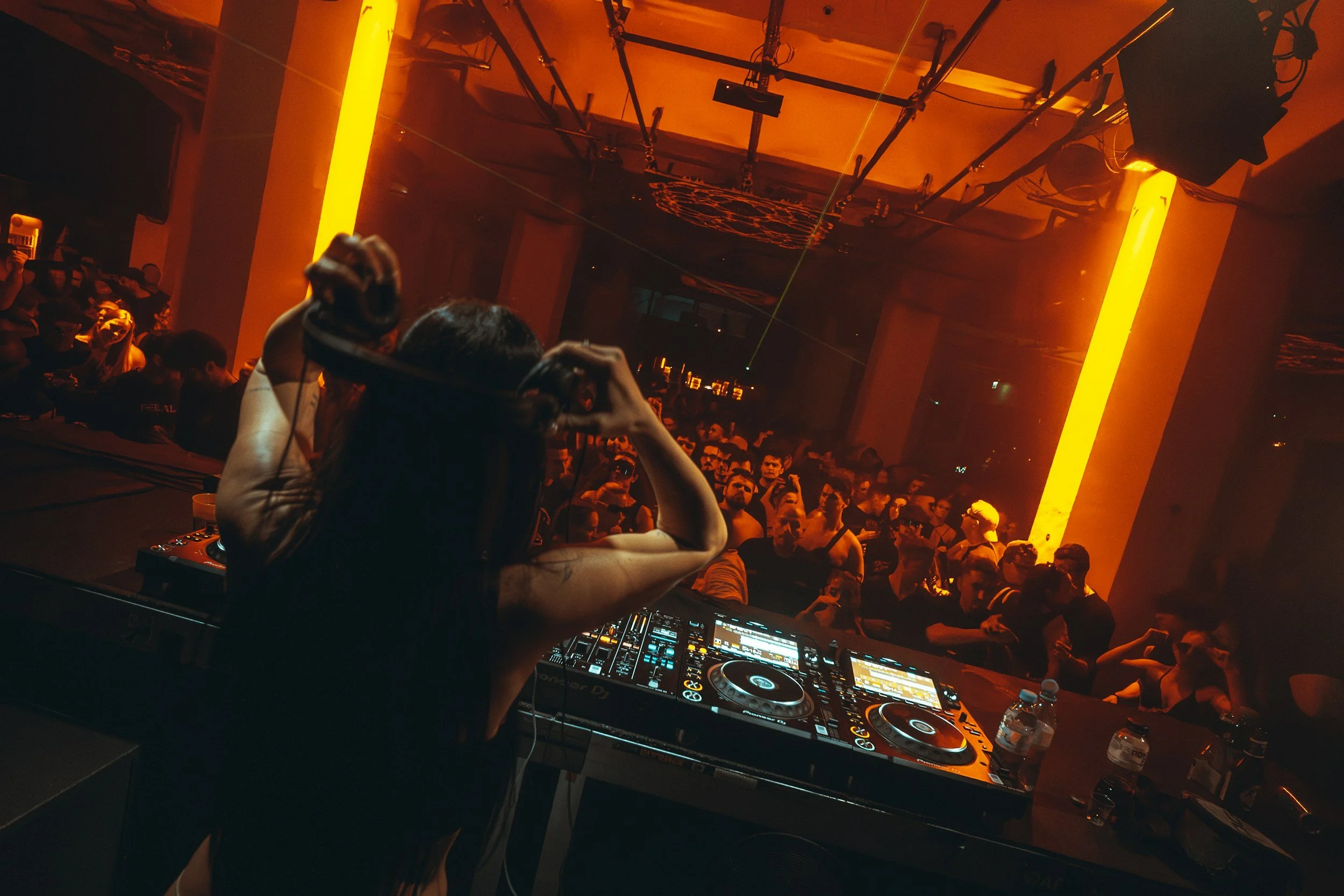 DJ performing at a crowded nightclub with turntables, orange lighting, and an enthusiastic dancing crowd