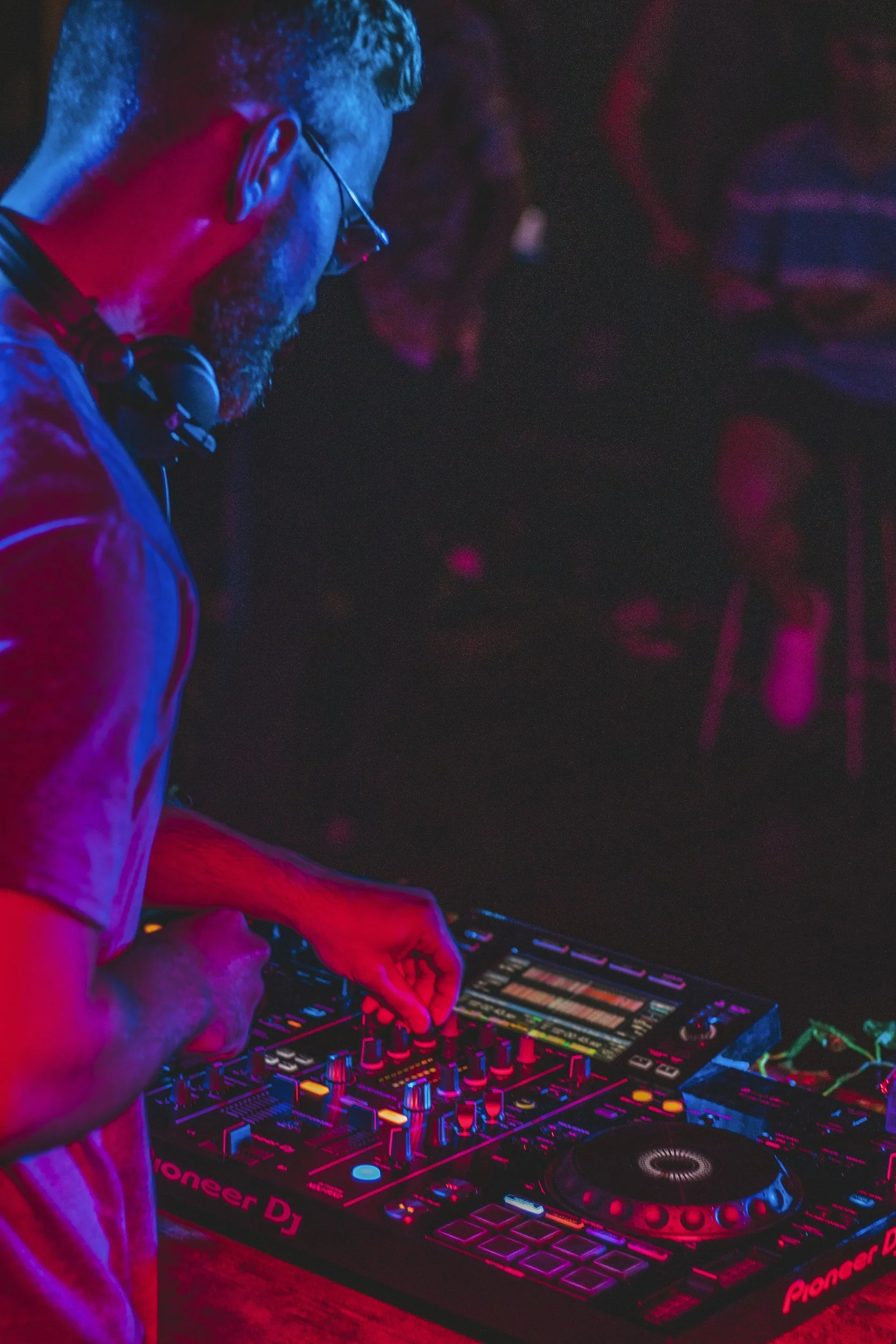 DJ adjusting a Pioneer DJ mixer and turntables under vibrant blue and magenta nightclub lighting