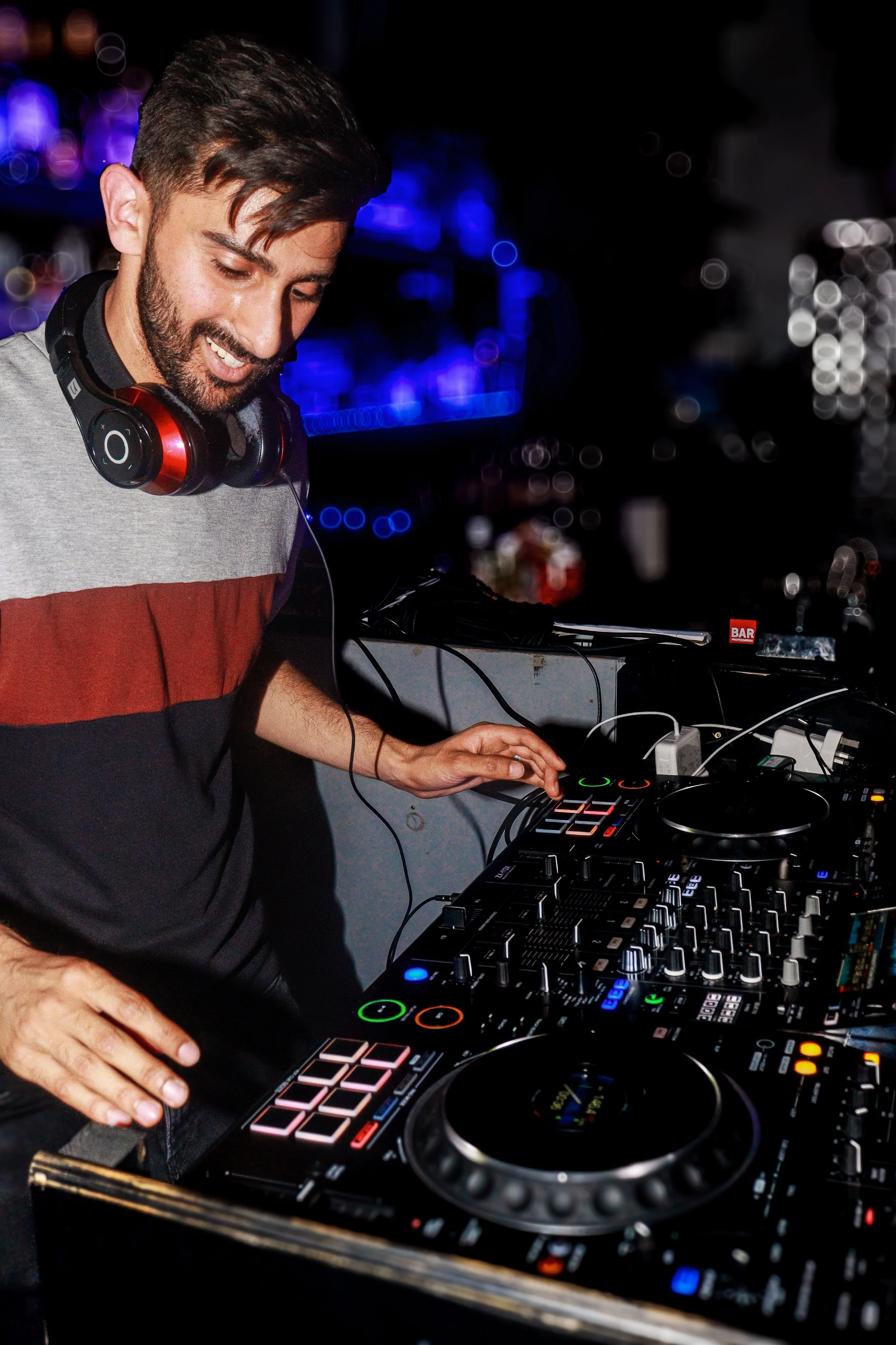 DJ wearing headphones operates a professional DJ mixer and turntables in a dark club with blue lighting.