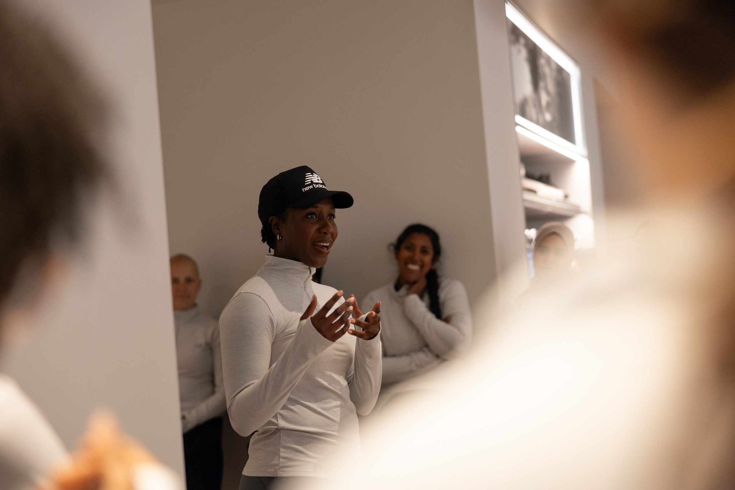 Woman wearing a New Balance cap speaking to a small group indoors
