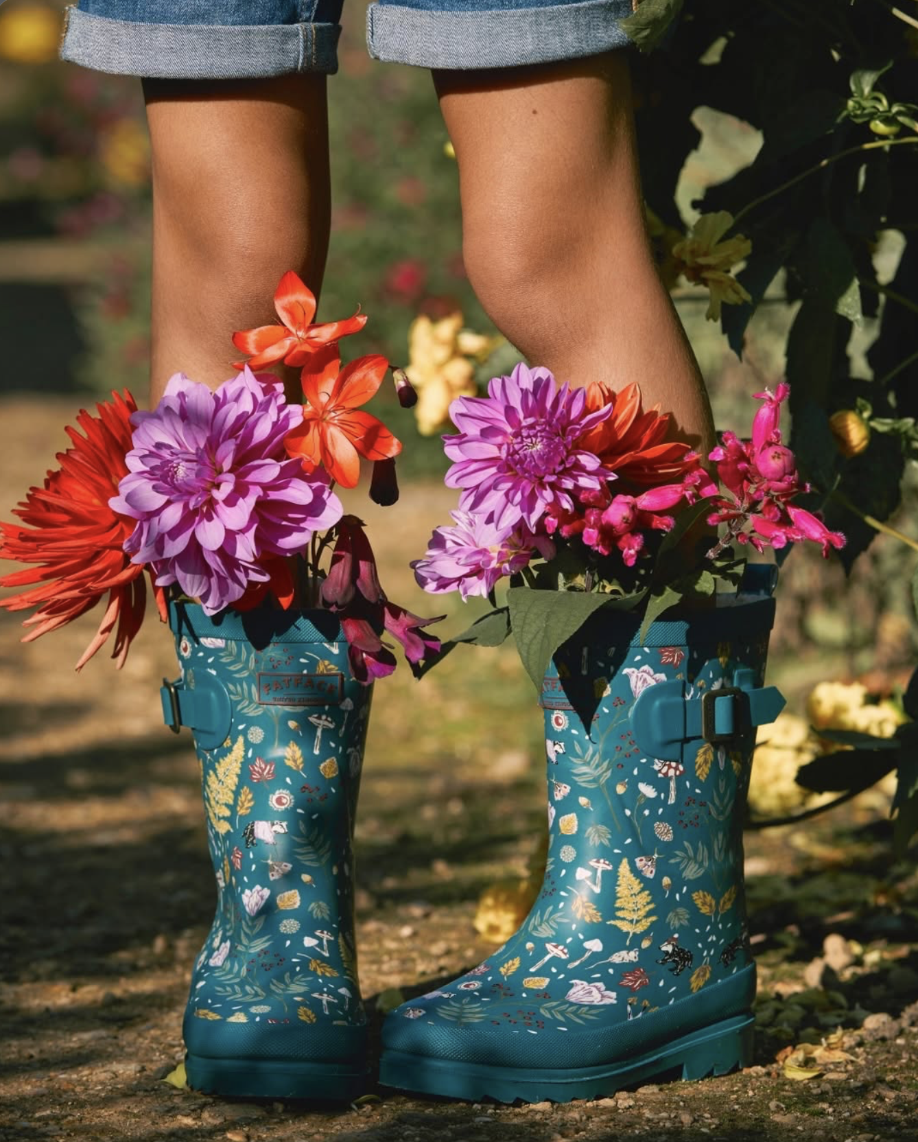 Person wearing patterned teal rain boots filled with colorful flowers in a garden. Hand painted surface print designs. Freelance print designer.