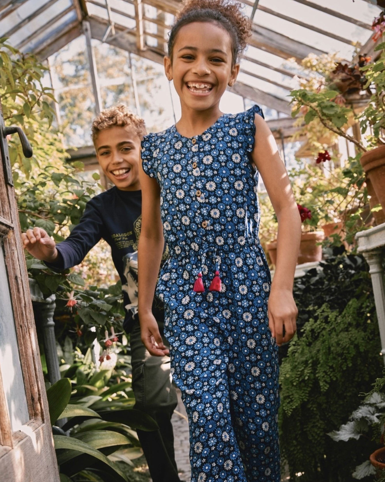 Smiling children standing among plants inside a sunlit greenhouse. Hand painted surface print designs. Freelance print designer.