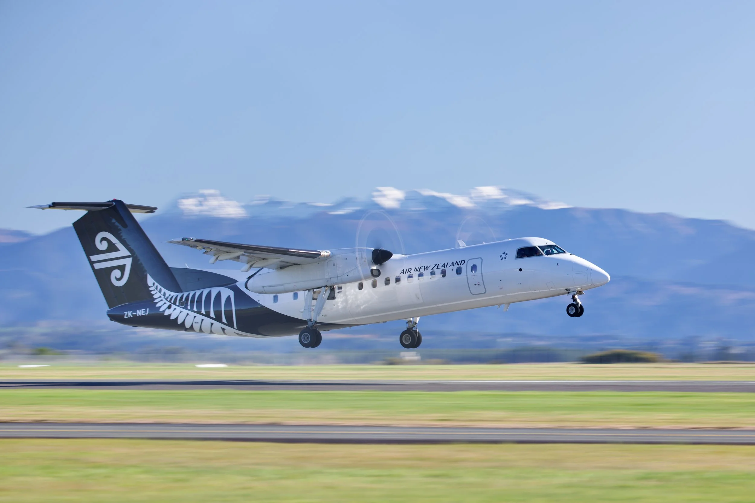 Air New Zealand turboprop passenger plane taking off over a runway with mountains in the background
