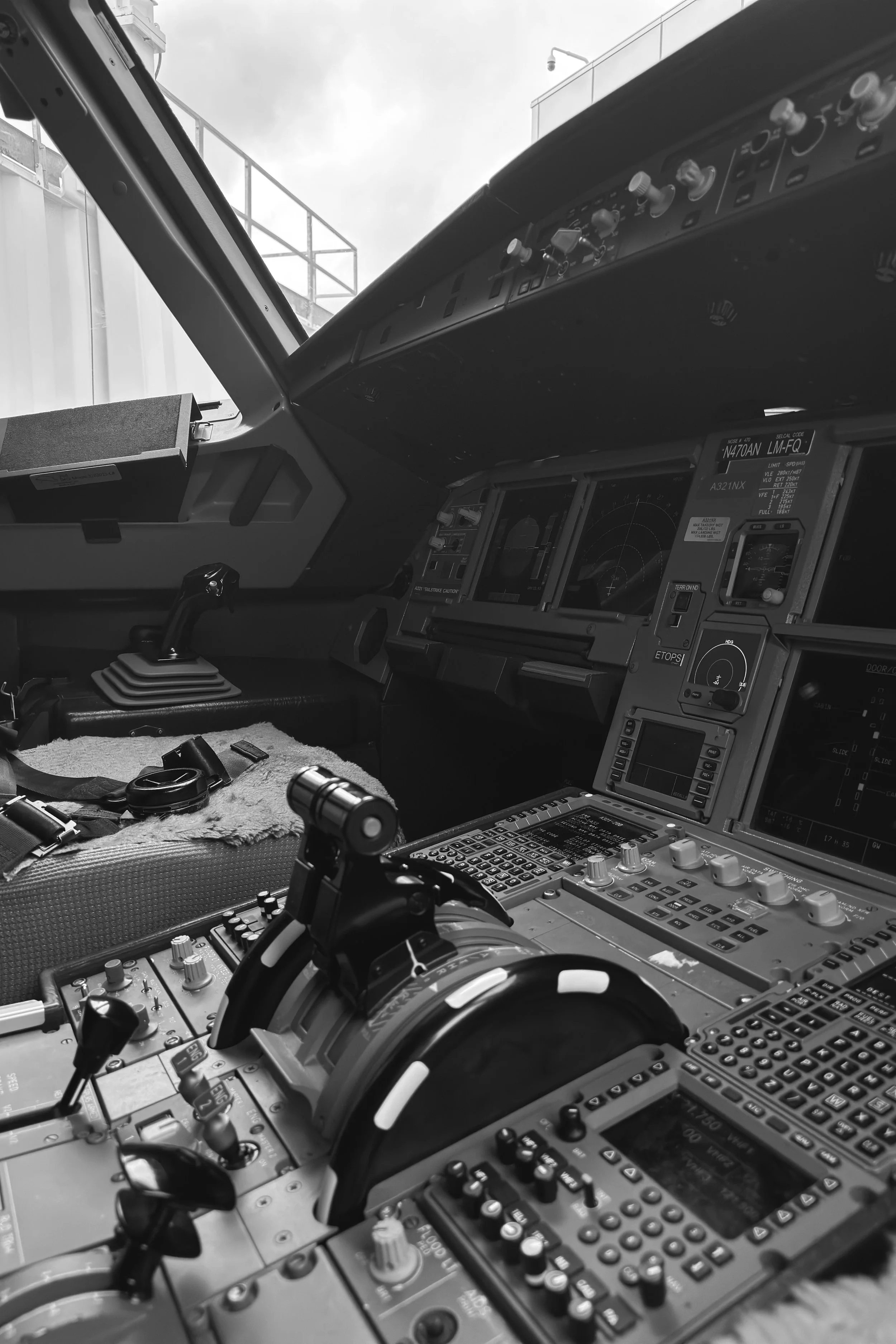 Black-and-white view of an Airbus A321 cockpit with flight controls, instrument panels, displays, and overhead switches.