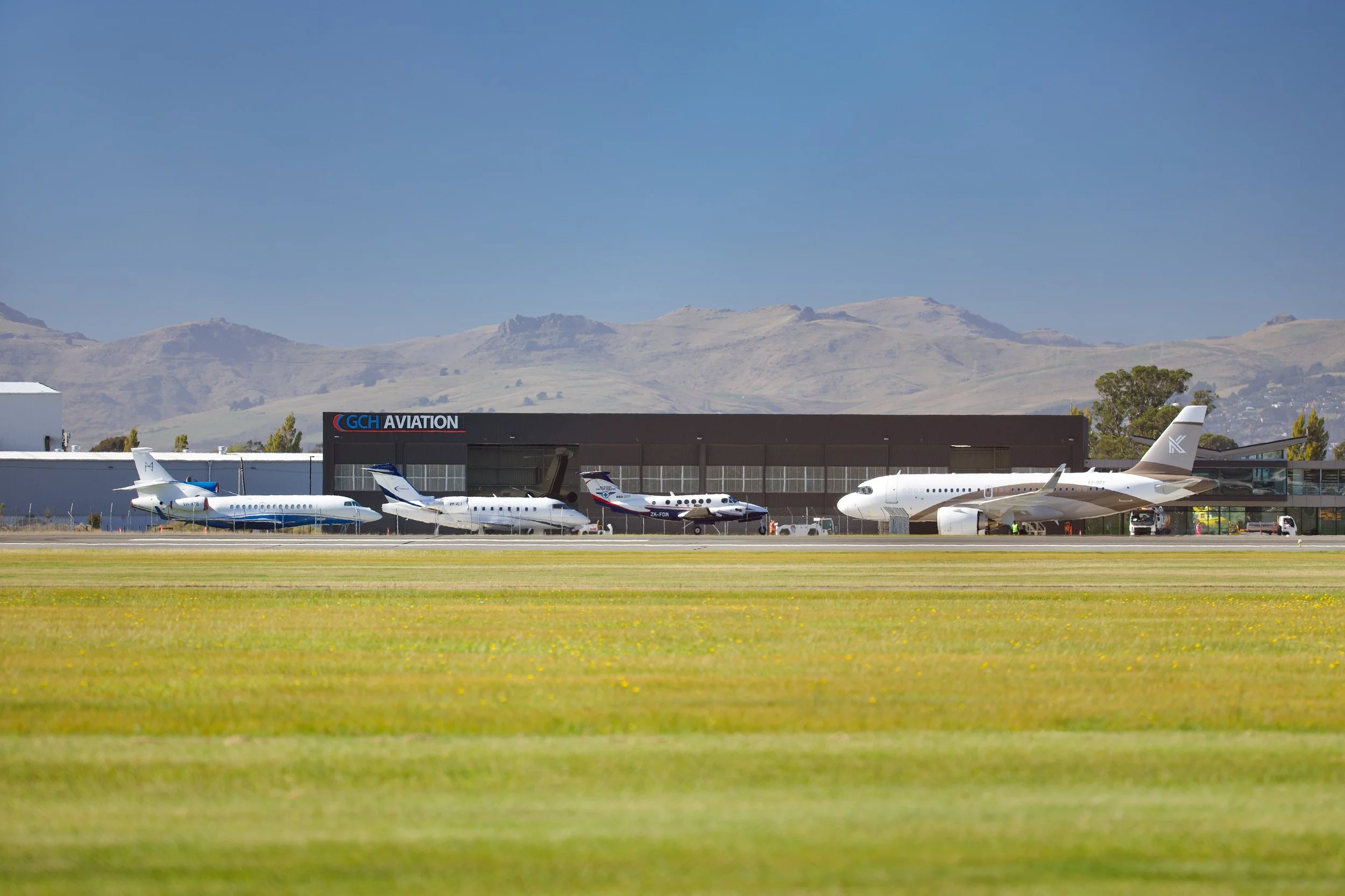 Several aircraft parked outside a GCH Aviation hangar with mountains in the background