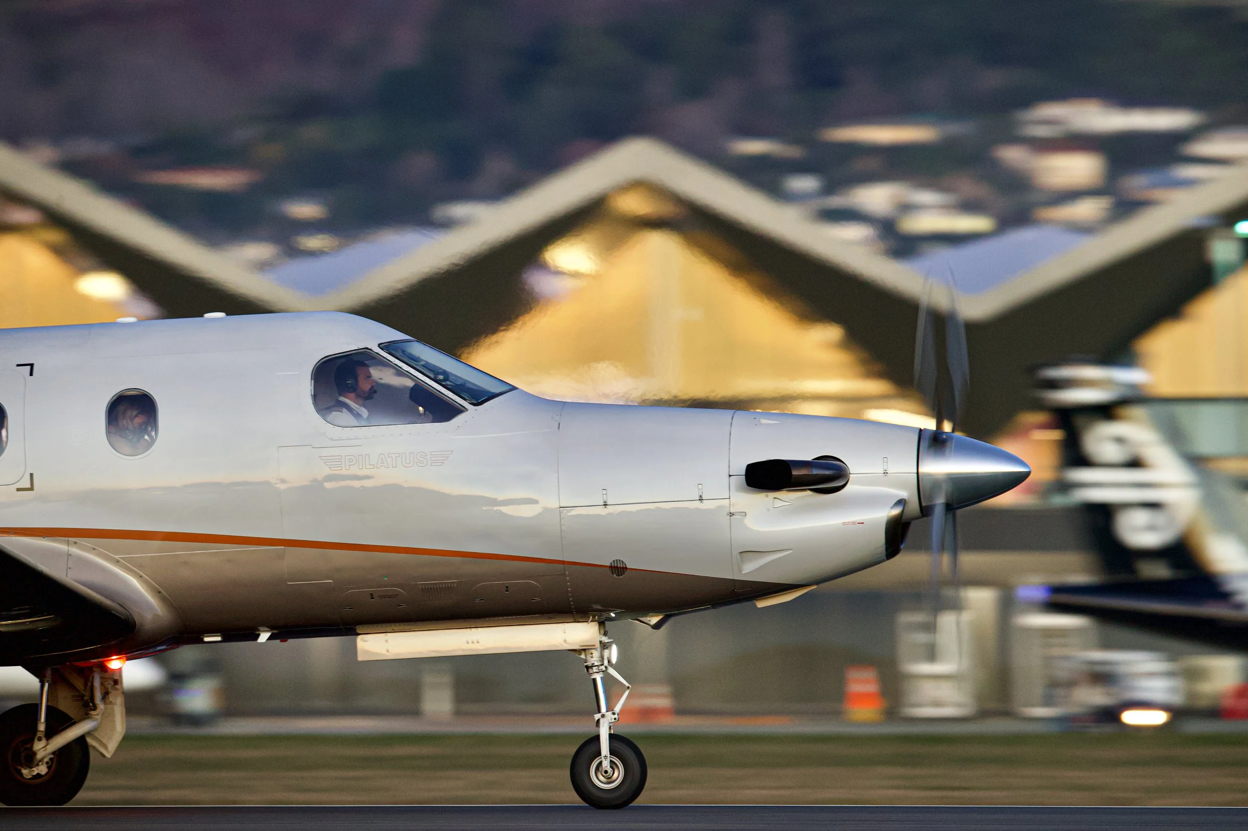 White Pilatus turboprop airplane taxiing on an airport runway with landing gear down