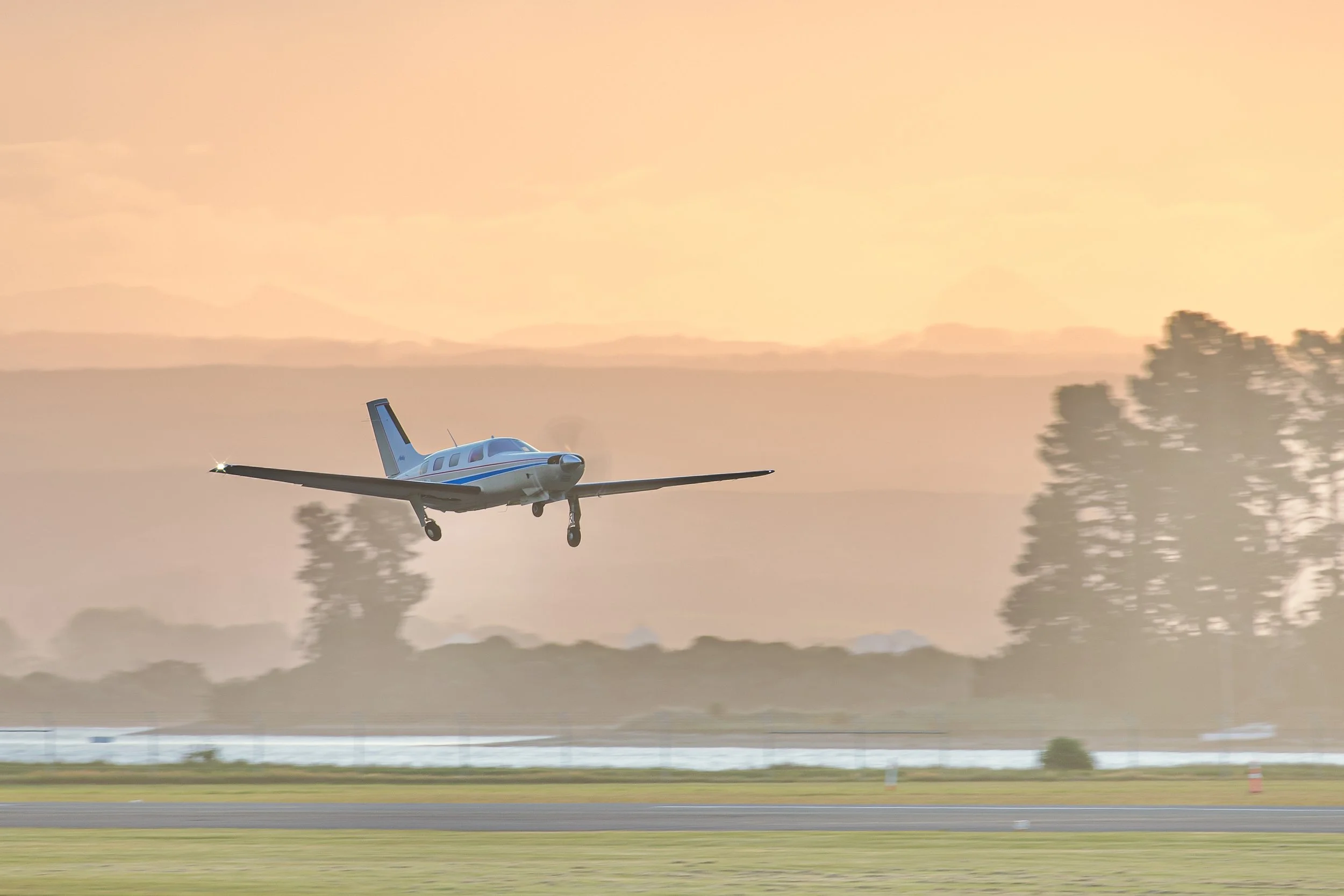 Small single-engine airplane landing on a runway at sunset with landing gear down