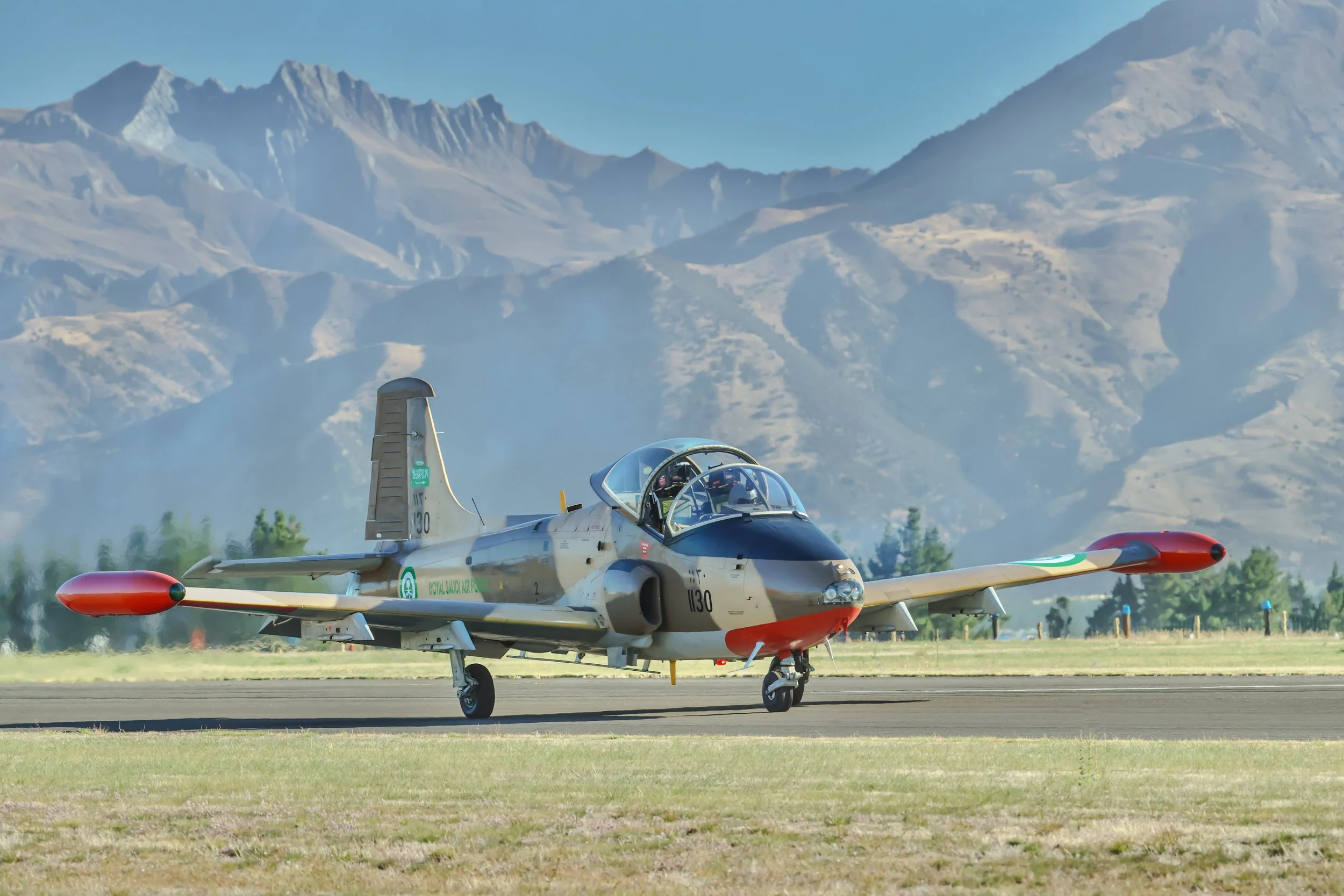 Military jet trainer parked on a runway with rugged mountains in the background