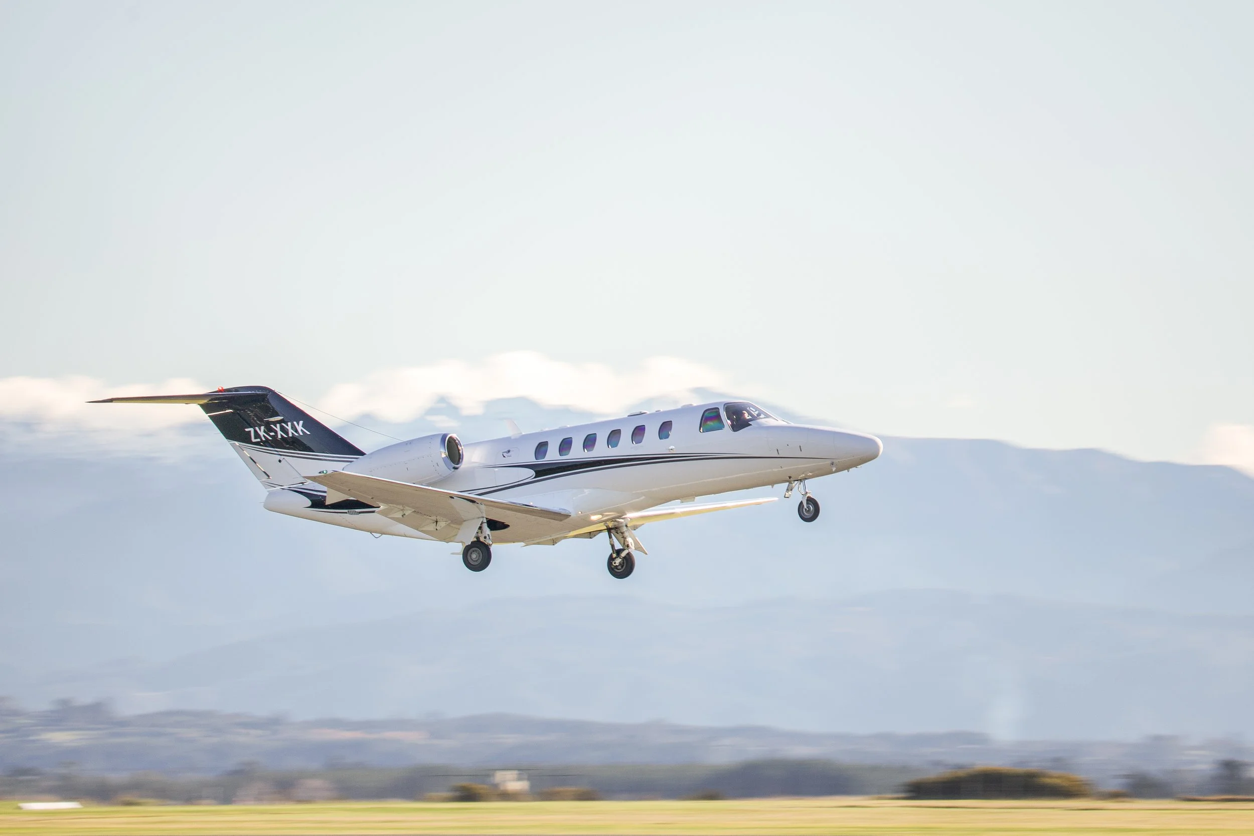 White private jet taking off above a runway with landing gear extended in Nelson Airport nz 