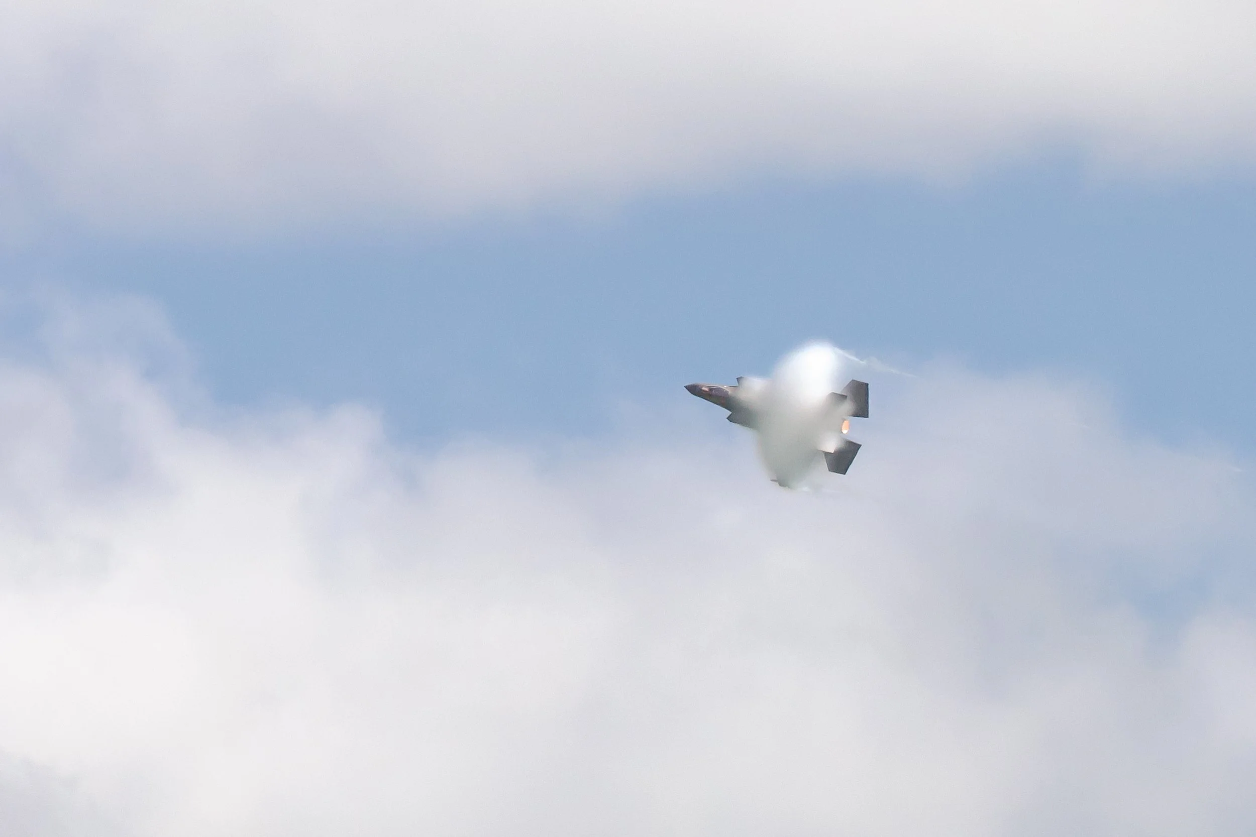 Stealth fighter jet flying through clouds with afterburner glowing