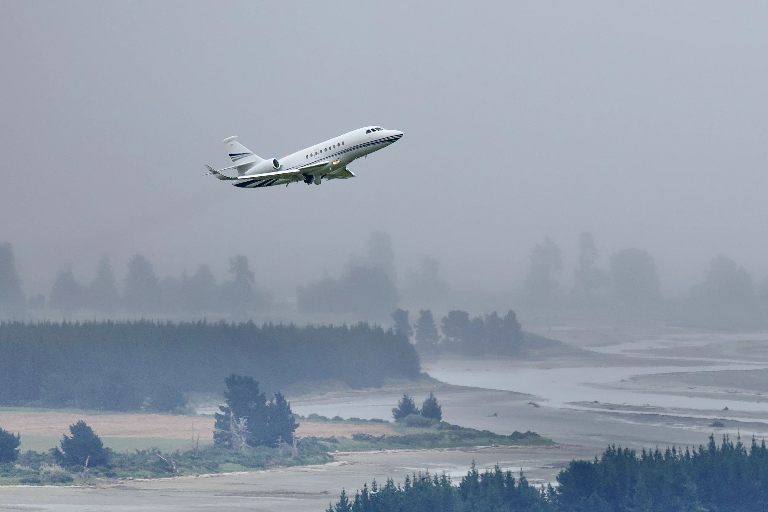 White private jet flying over a misty forest and winding river
