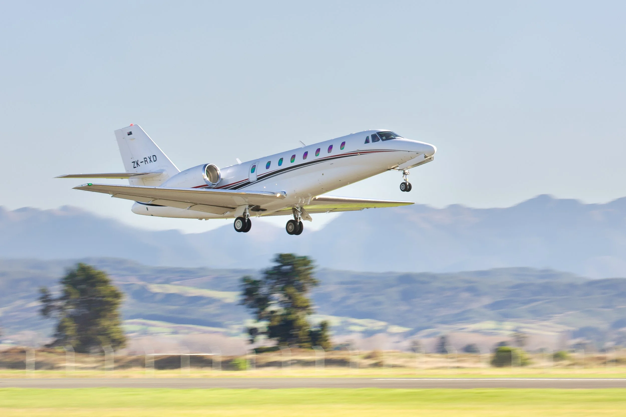 White twin-engine private jet taking off with landing gear extended above a runway