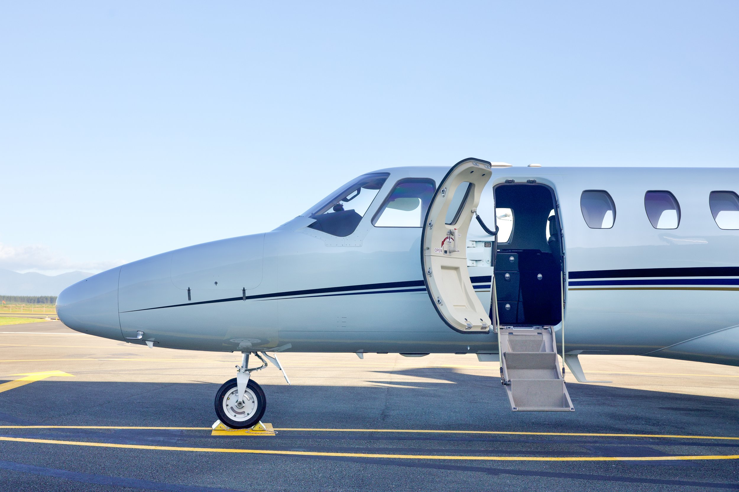 Private jet with open cabin door and stairs parked on an airport runway