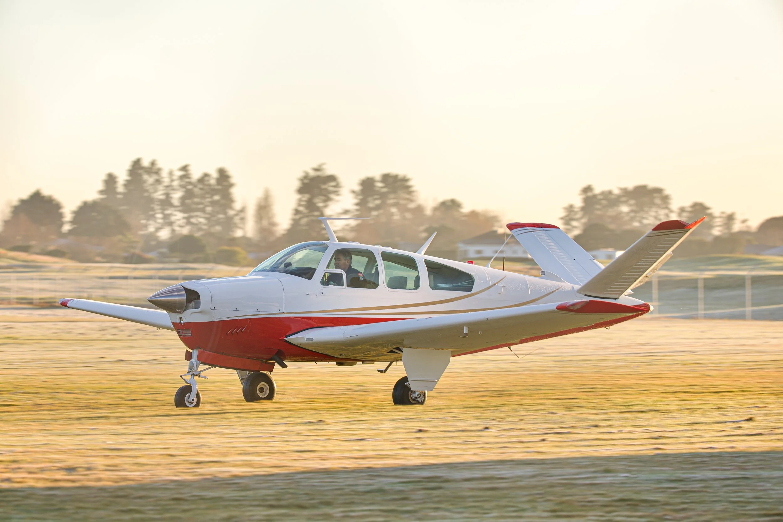 Red-and-white single-engine propeller airplane taxiing on a grassy airfield at sunset