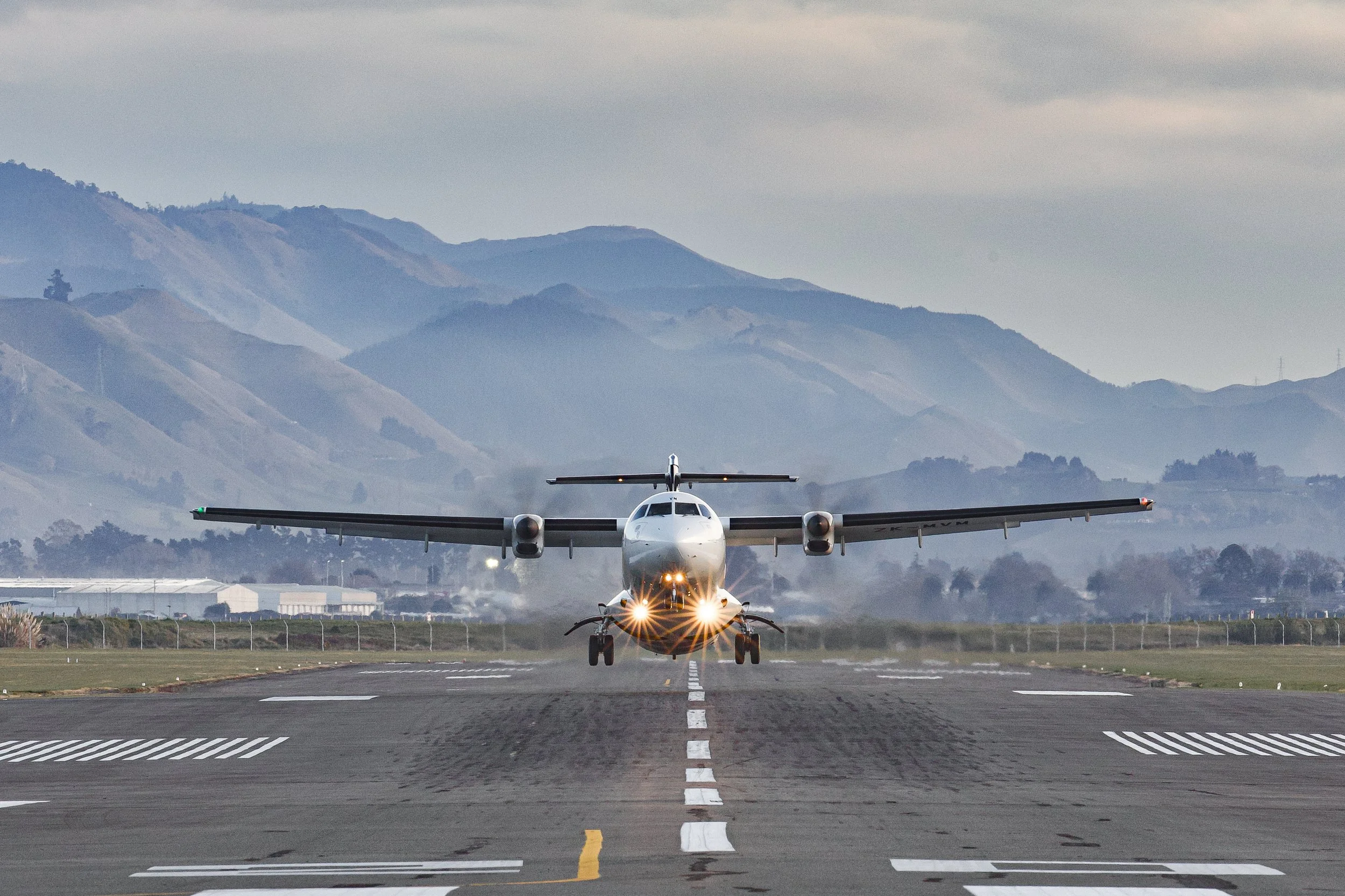 Twin-engine turboprop airplane taking off from a runway with mountains in the background