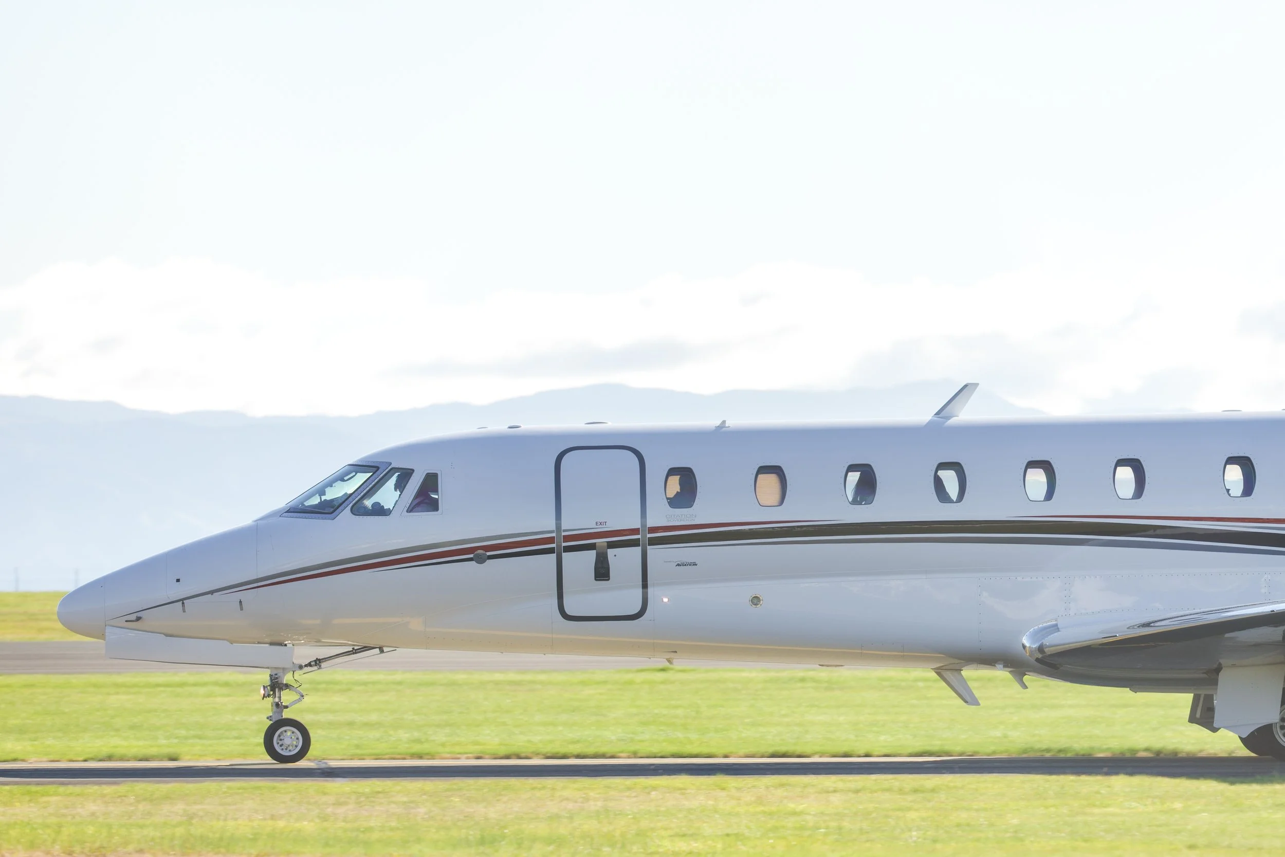 Side view of a white private jet taxiing on a runway with landing gear extended