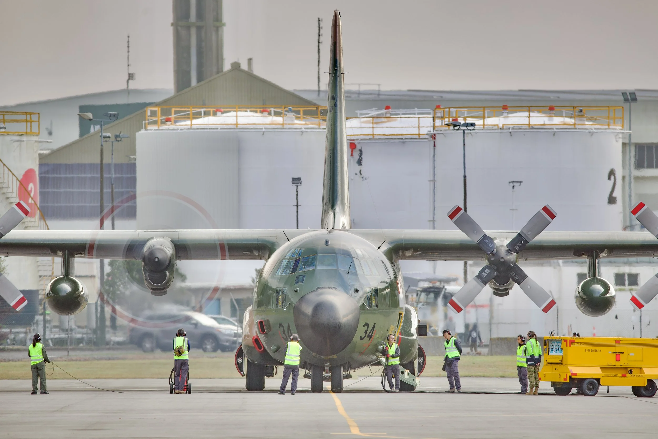 Front view of a four-engine military transport aircraft with propellers, surrounded by ground crew on an airfield.