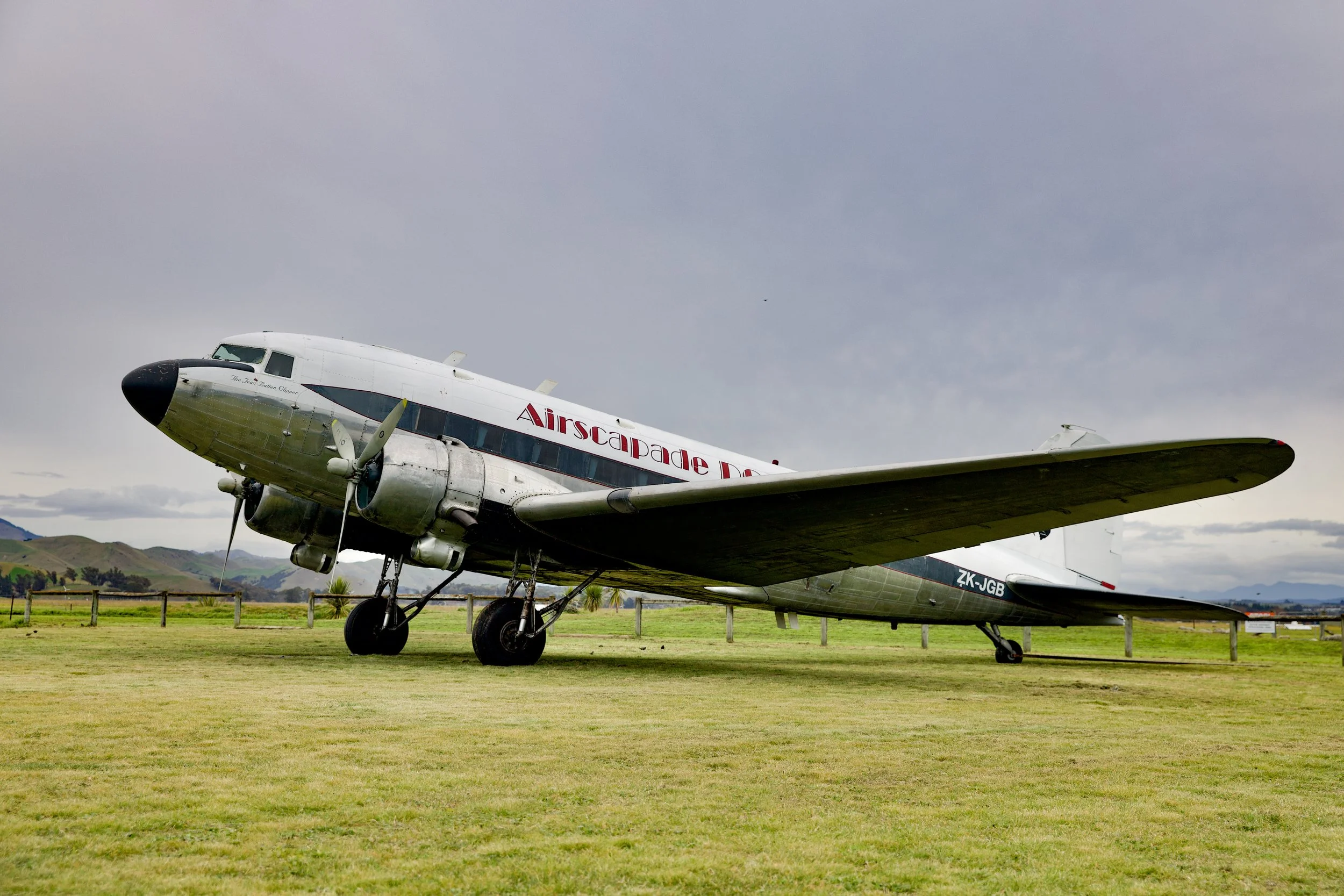 Vintage Airscapade DC-3 airplane parked on a grassy field with mountains in the background