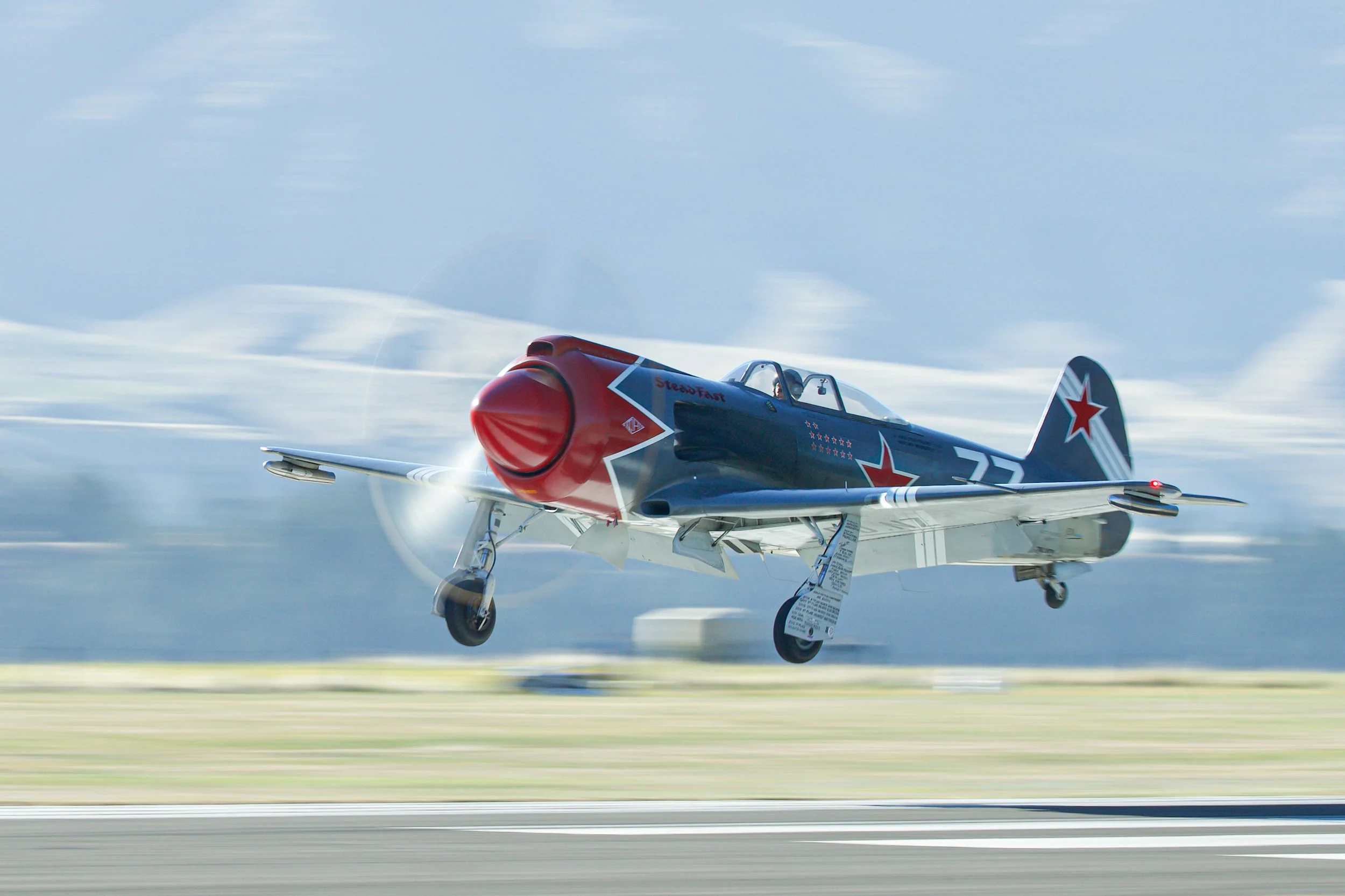 Vintage red, white, and blue propeller airplane taking off above a runway