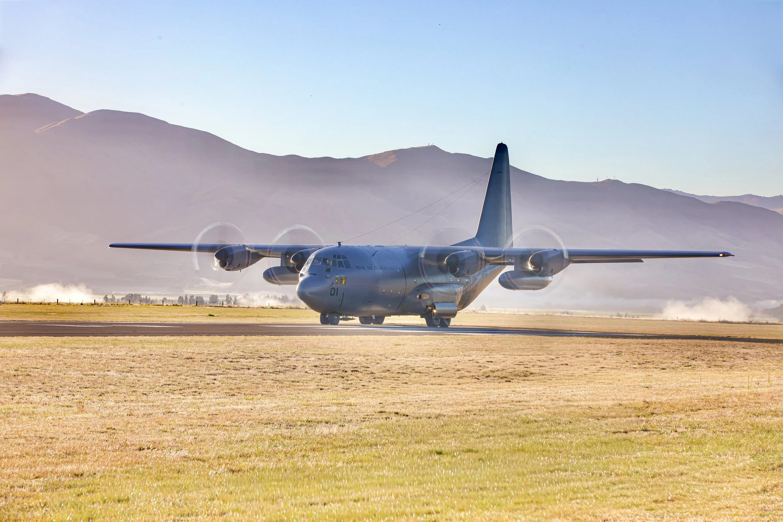 Royal New Zealand Air Force C-130 Hercules military transport aircraft landing on a runway with mountains in the background