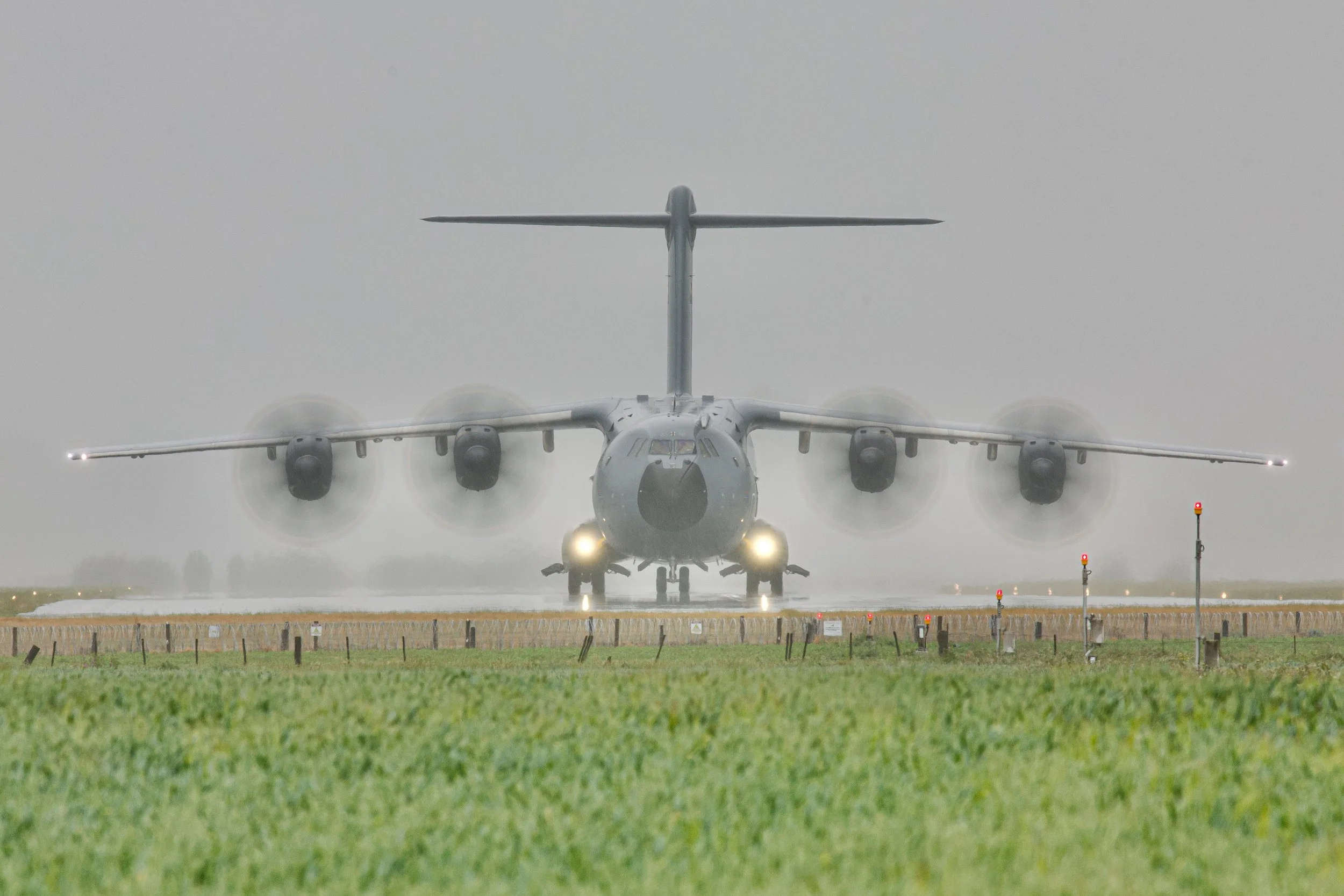 Four-engine military transport aircraft taking off on a rainy runway