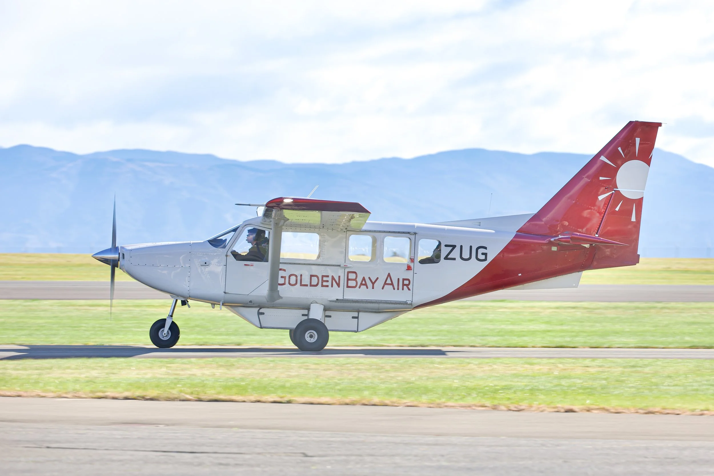 Golden Bay Air single-engine passenger plane taxiing on a runway with mountains in the background