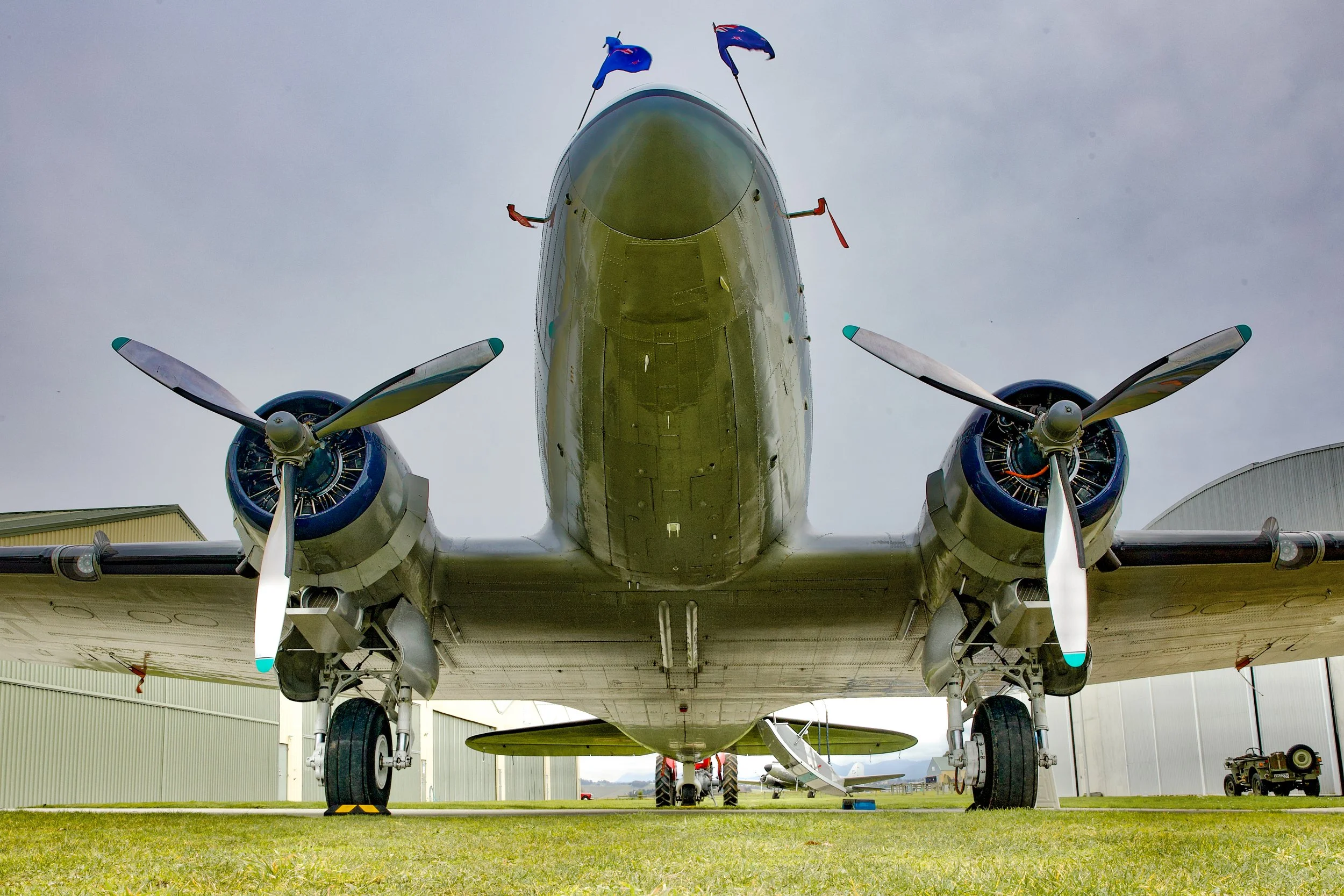 Low-angle view of a vintage twin-engine military transport aircraft with blue propellers parked outside an aircraft hangar