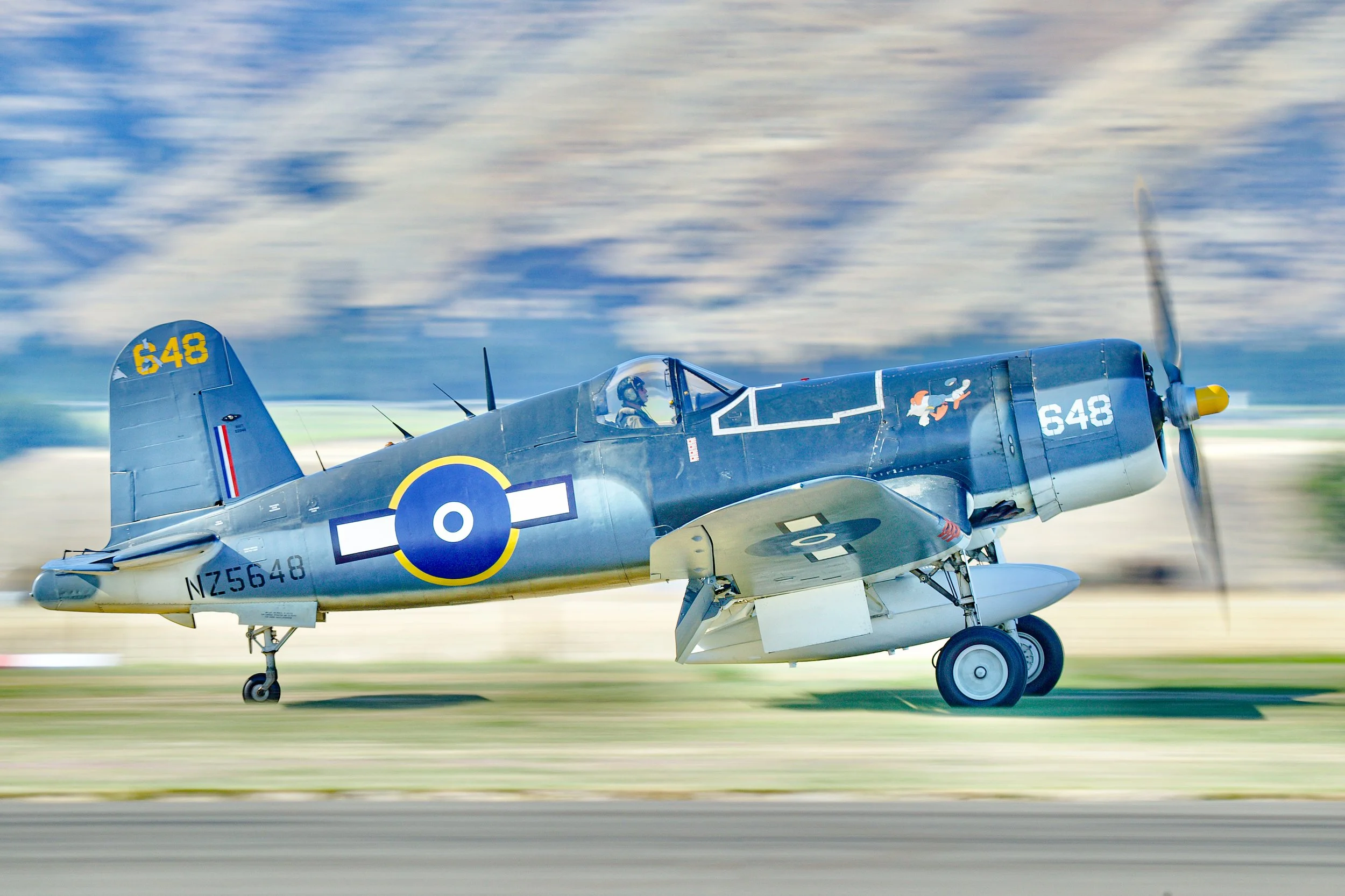 Vintage blue World War II-era fighter plane with British roundel and tail number 648 taking off on a runway.