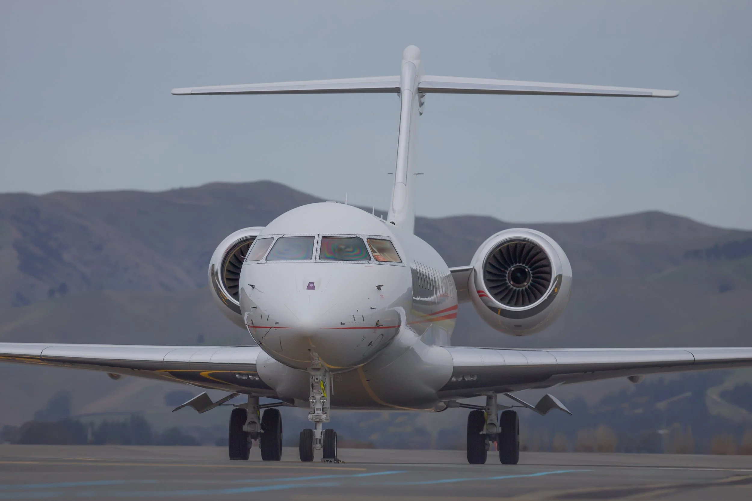 Front view of a white twin-engine business jet on a runway with mountains in the background