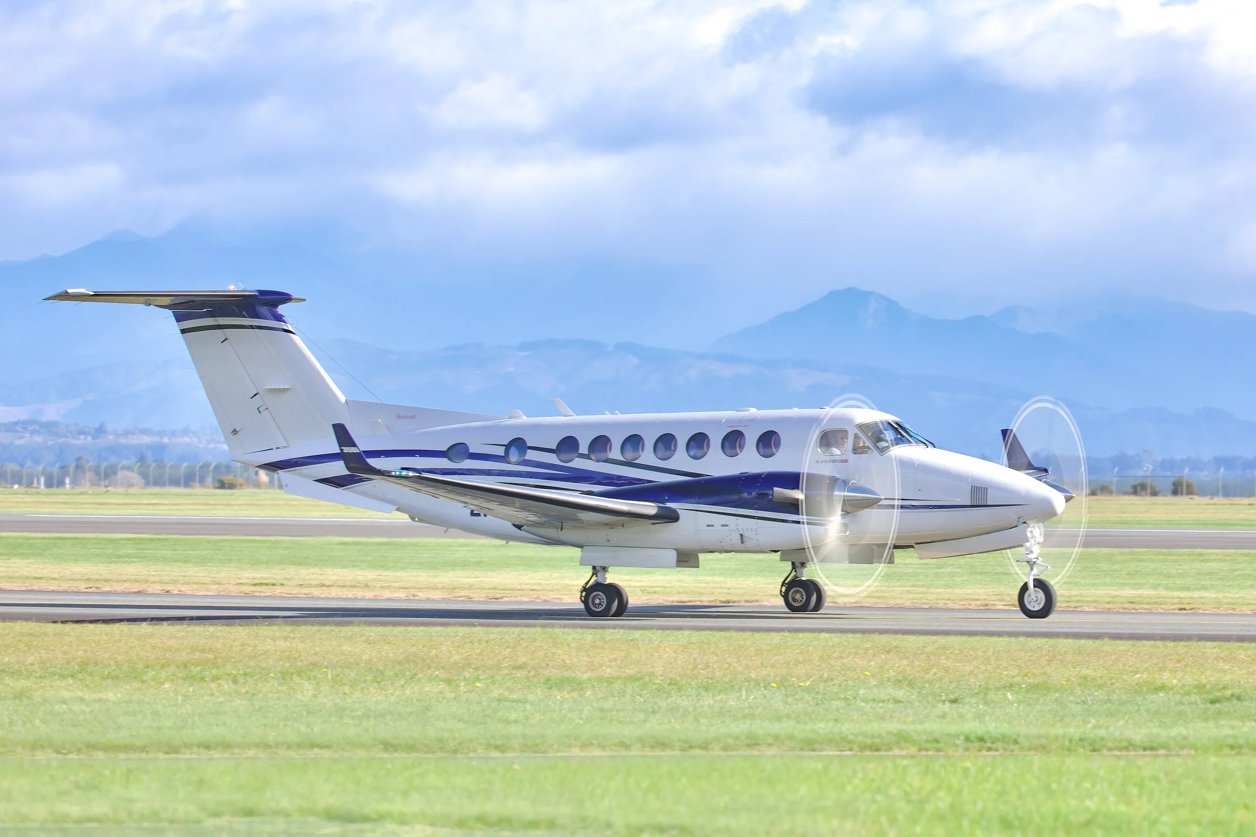 Twin-engine turboprop passenger aircraft taxiing on a runway with mountains in the background