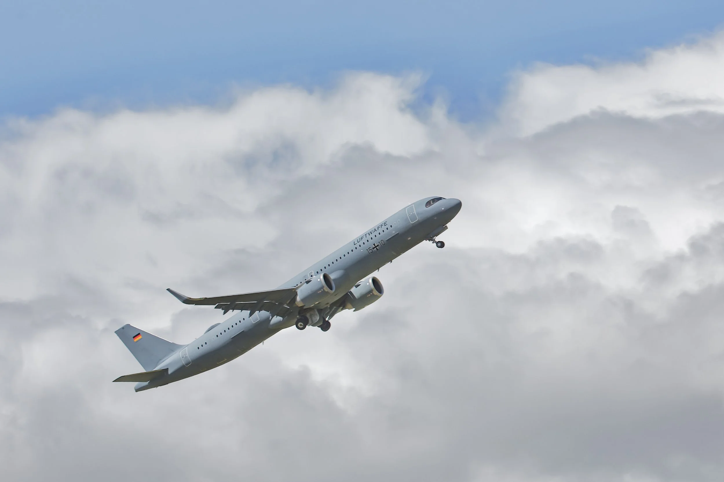 Lufthansa passenger airplane climbing through cloudy blue skies with landing gear extended