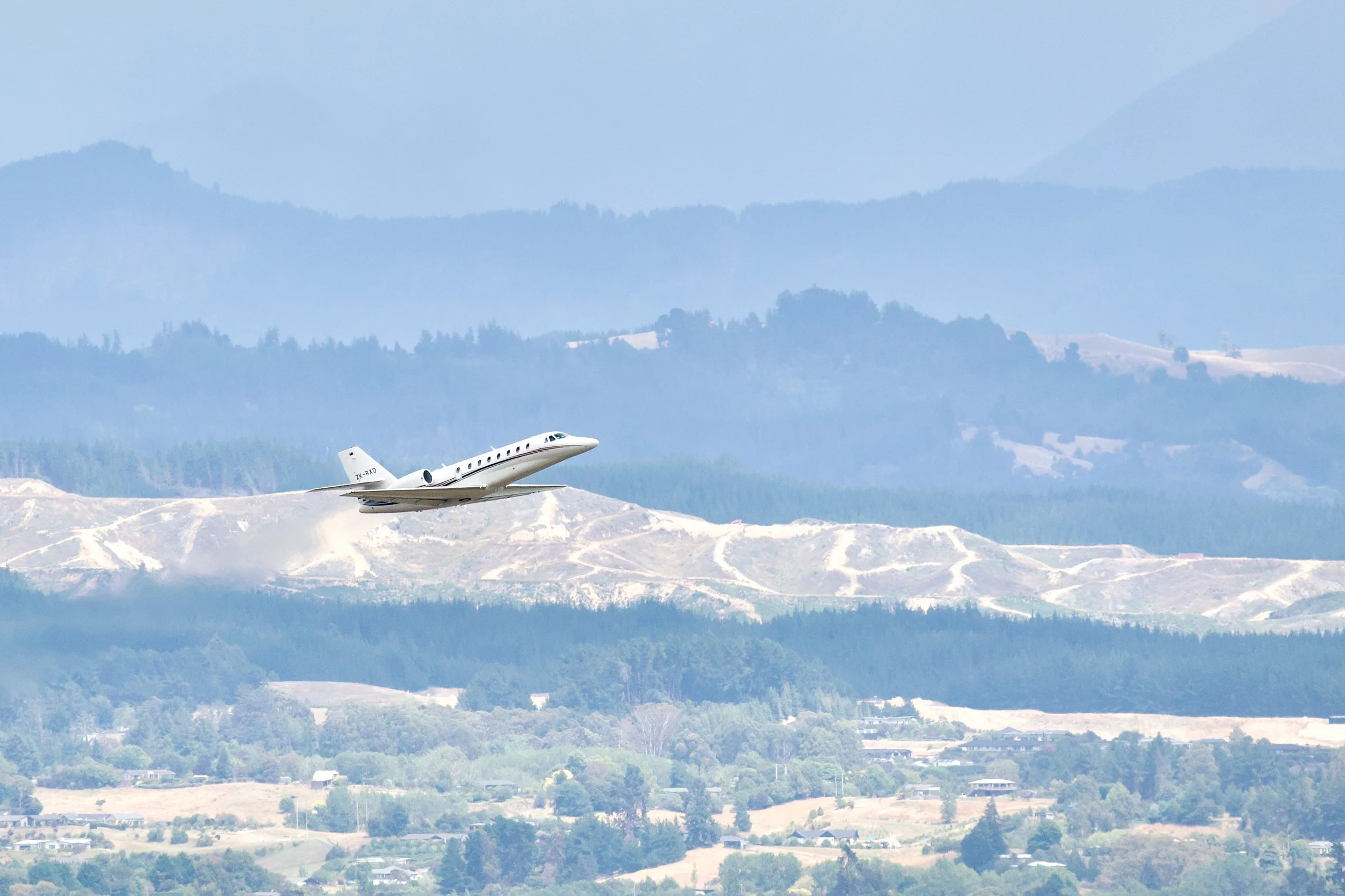 White private jet flying over snow-covered mountains and forested hills