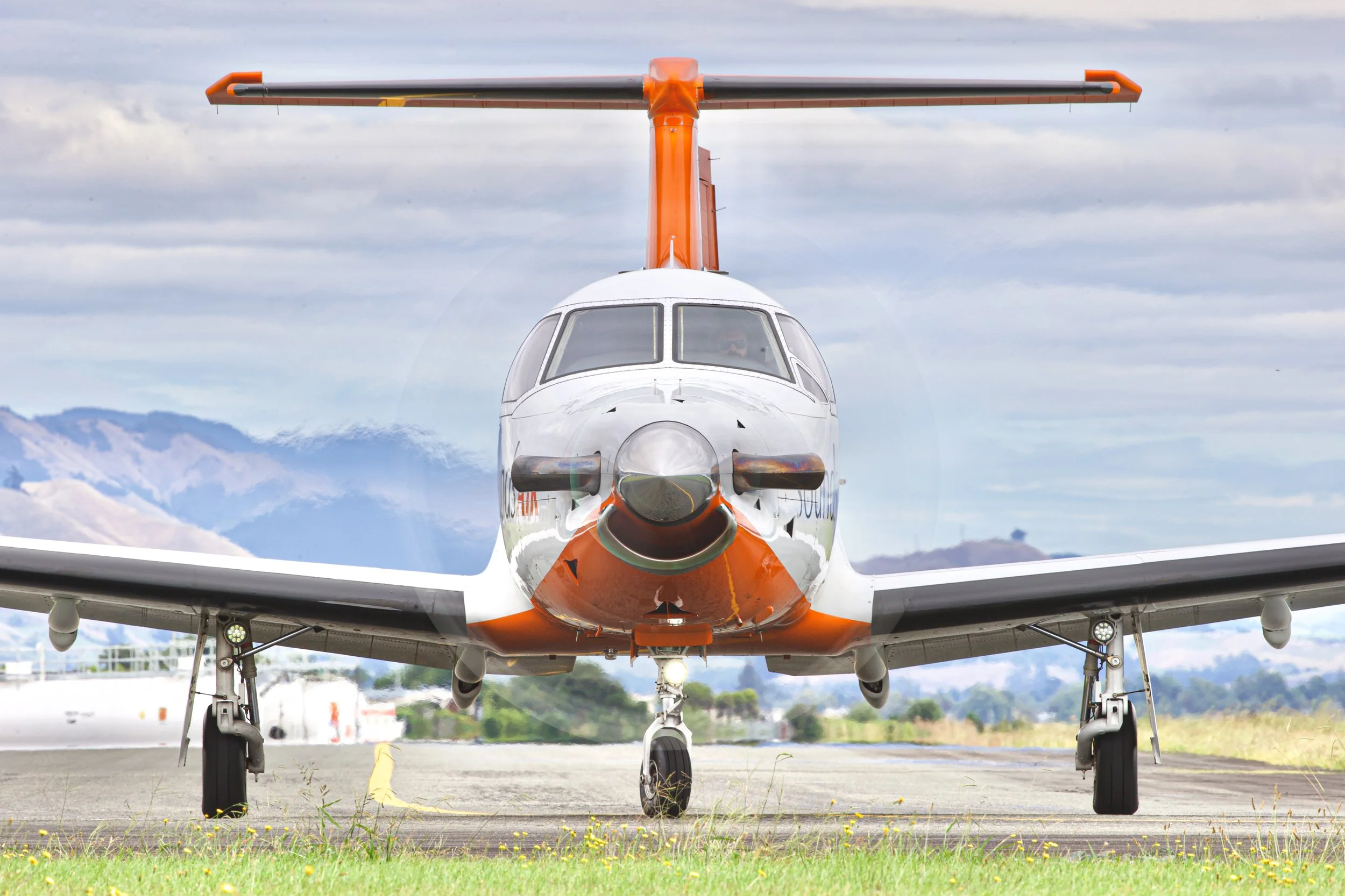 Front view of a vintage orange-and-white propeller airplane parked on a runway