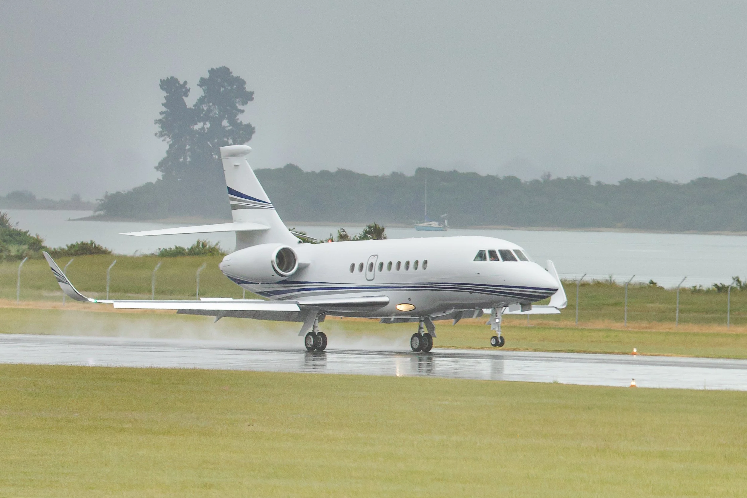 White private jet landing on a wet runway beside a lake in rainy weather