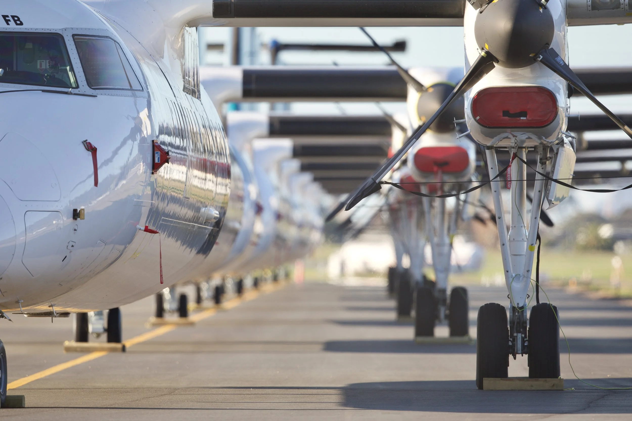 Small aircraft parked in a row on an airport apron, viewed from the front and side