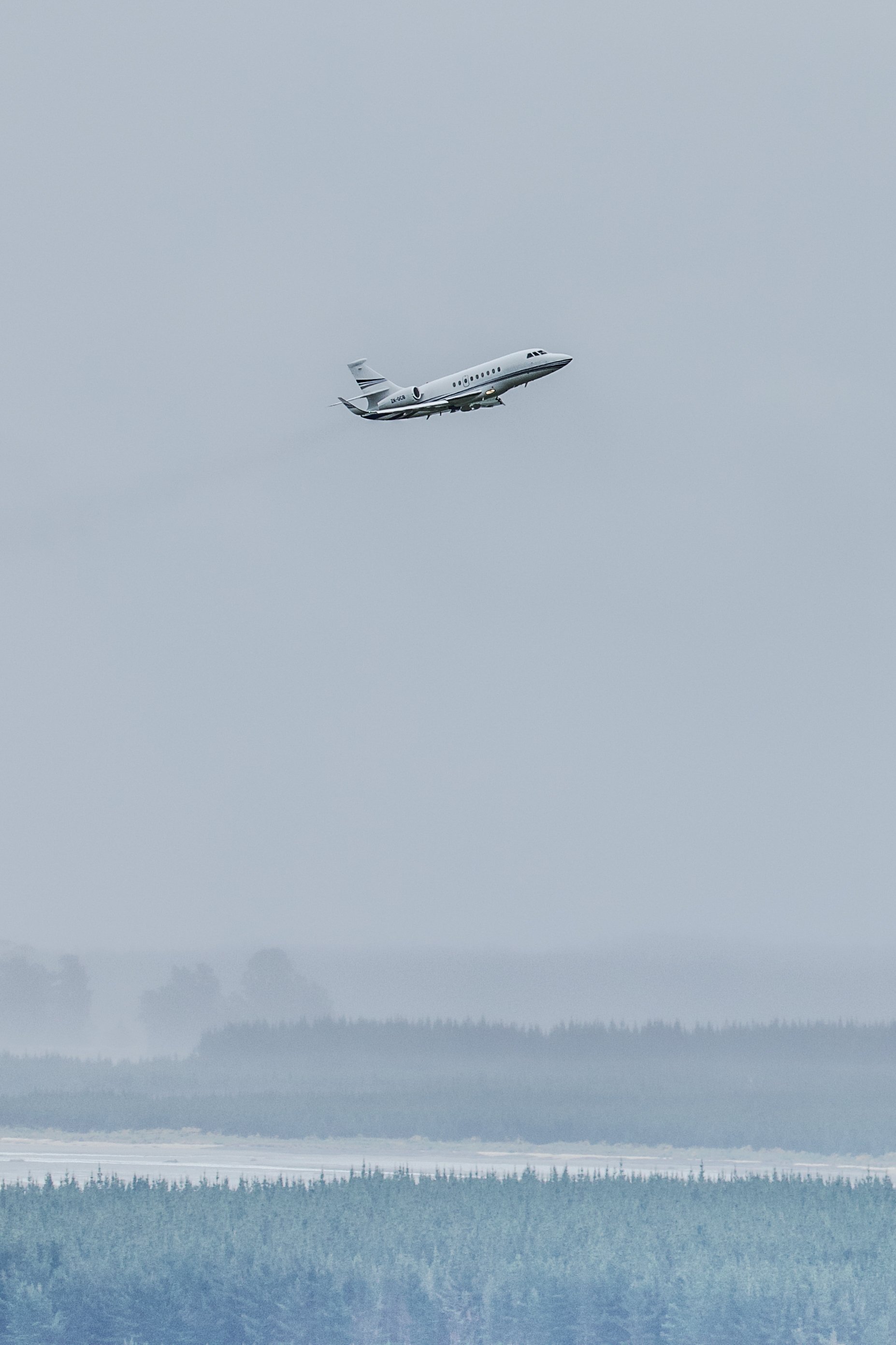 Private jet flying over a misty forest landscape